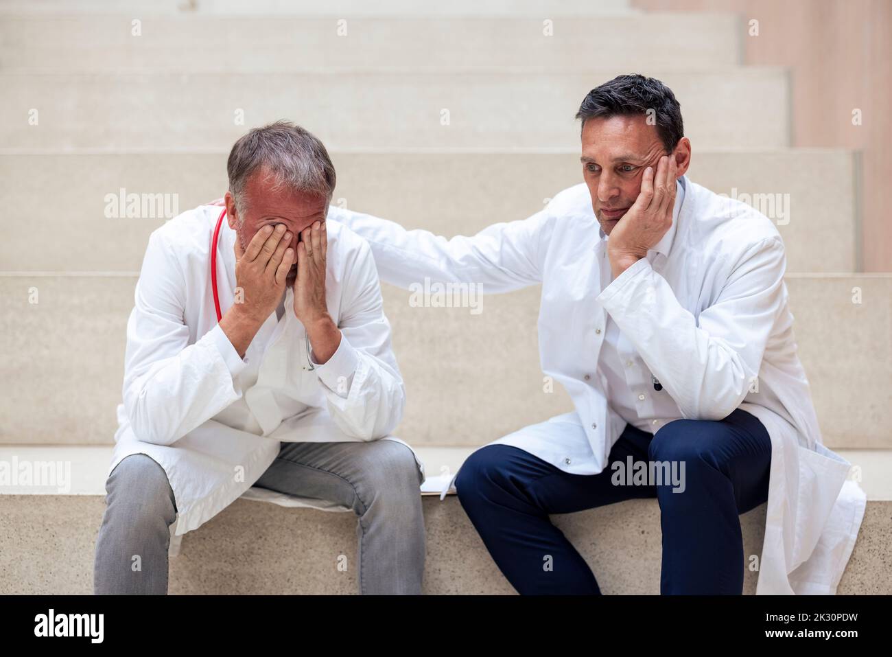 Un médecin se consolant a contrarié un collègue assis sur des marches à l'hôpital Banque D'Images