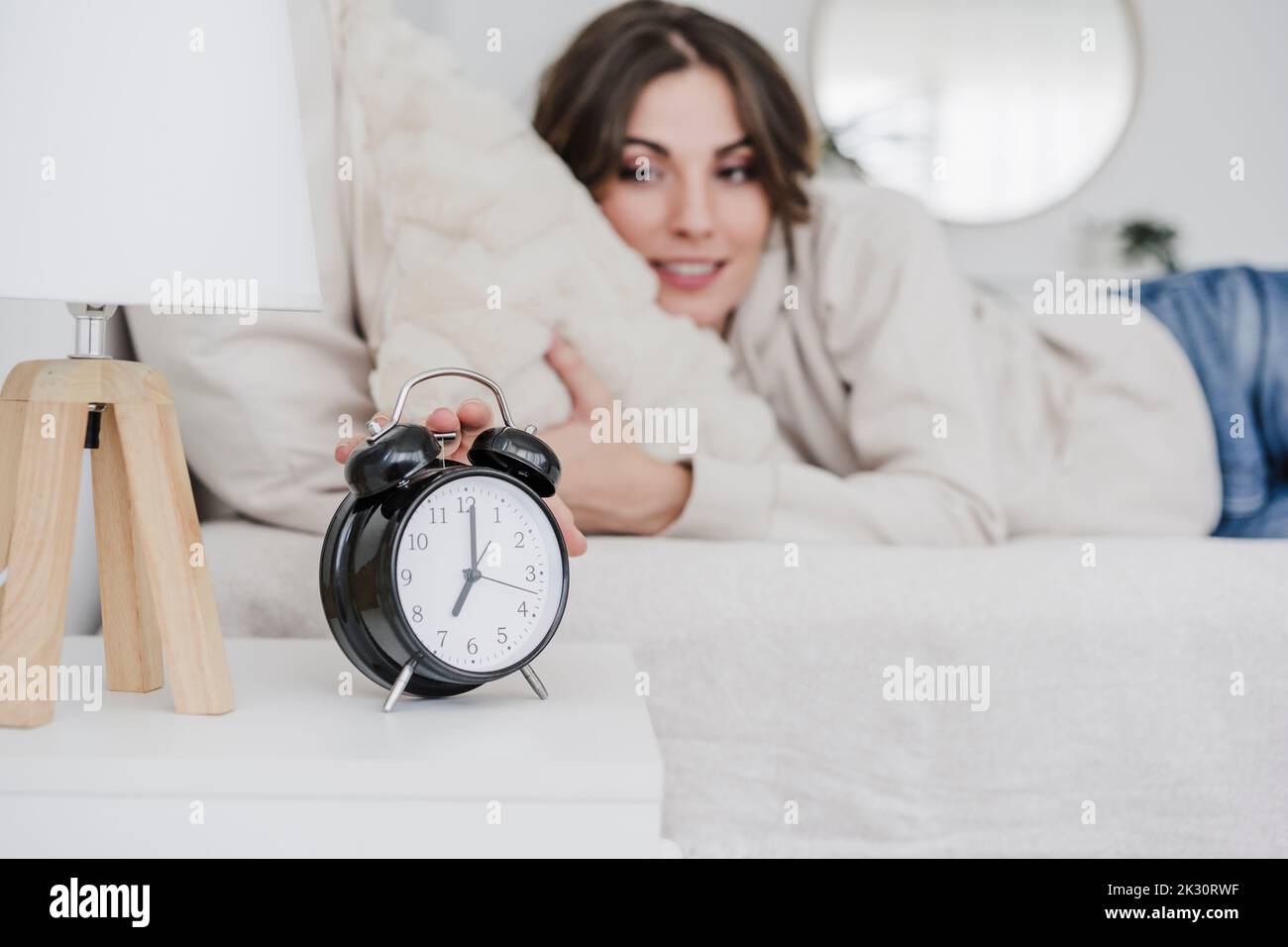 Jeune femme couché sur le lit et éteignant le réveil Banque D'Images