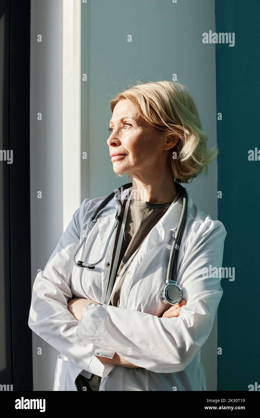 Médecin attentif debout avec les bras croisés par le mur Banque D'Images