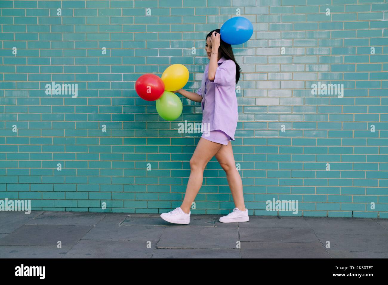 Jeune femme avec des ballons multicolores marchant par le mur Banque D'Images