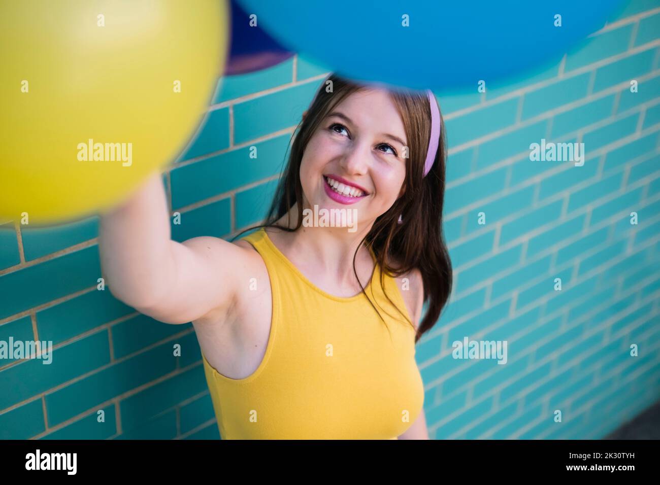 Femme souriante regardant des ballons multicolores par mur Banque D'Images