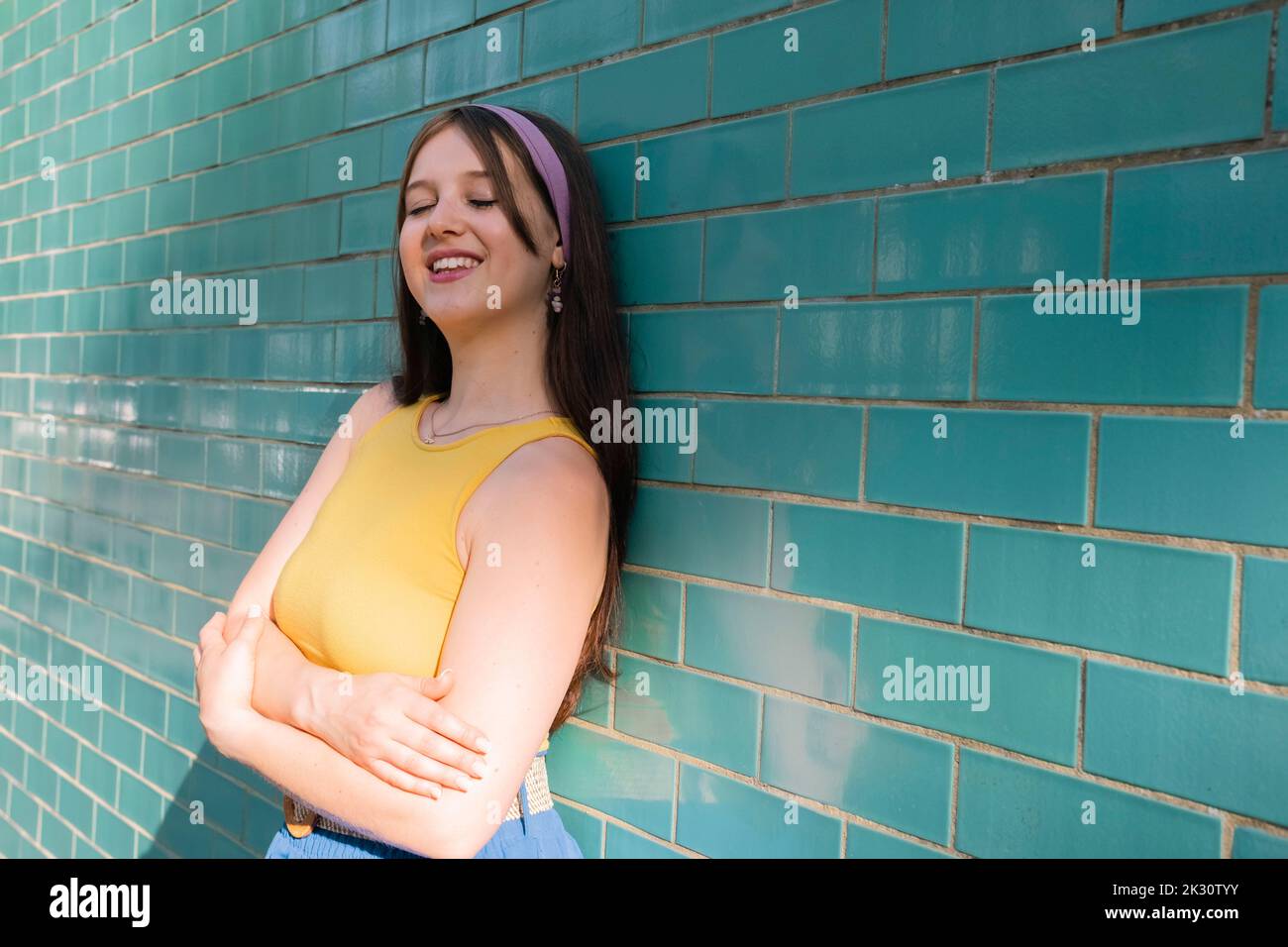 Femme souriante, les yeux fermés, penchée sur le mur du sarcelle Banque D'Images