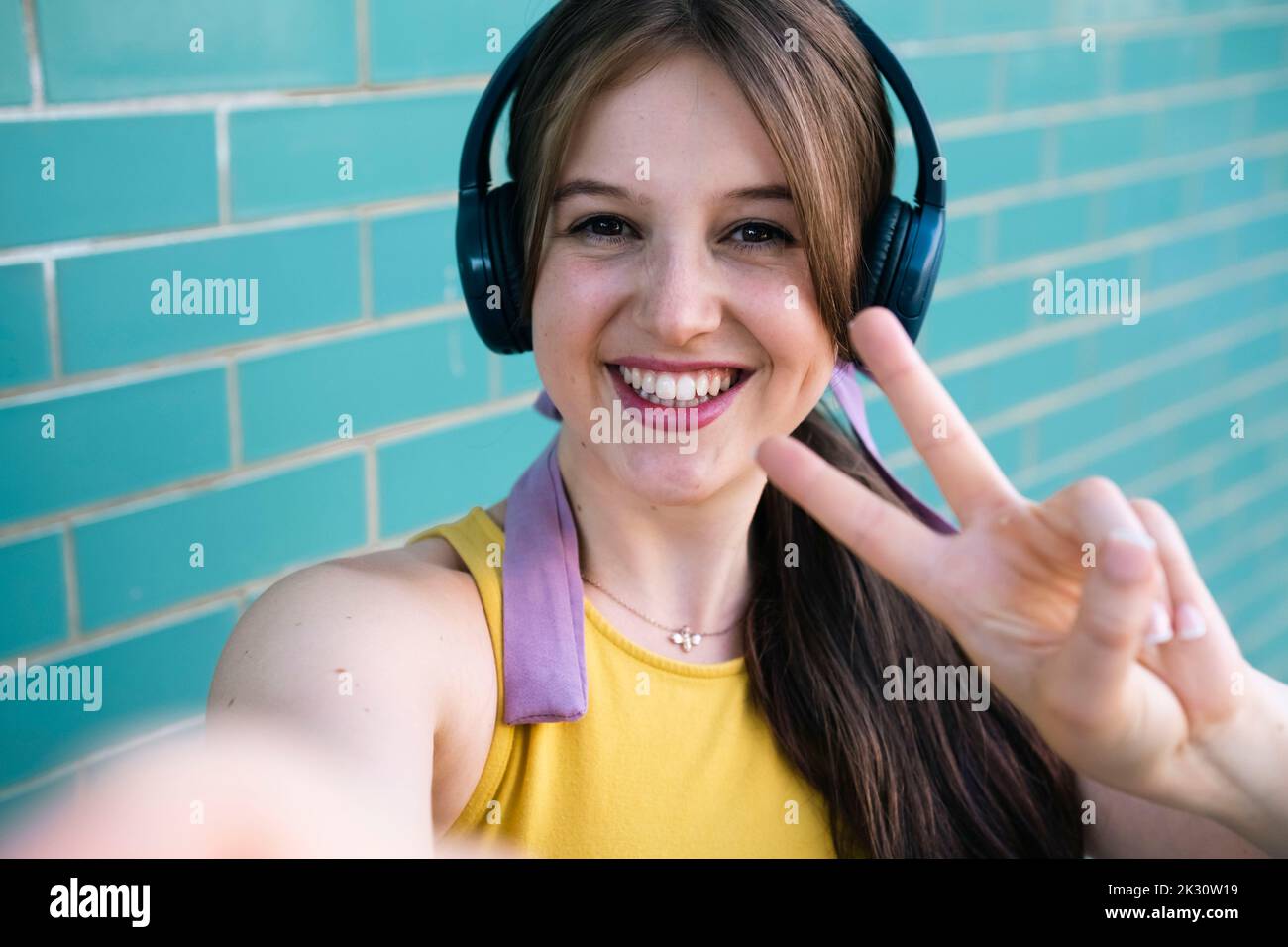 Une femme heureuse avec un casque montrant le signe de paix près du mur sarcelle Banque D'Images