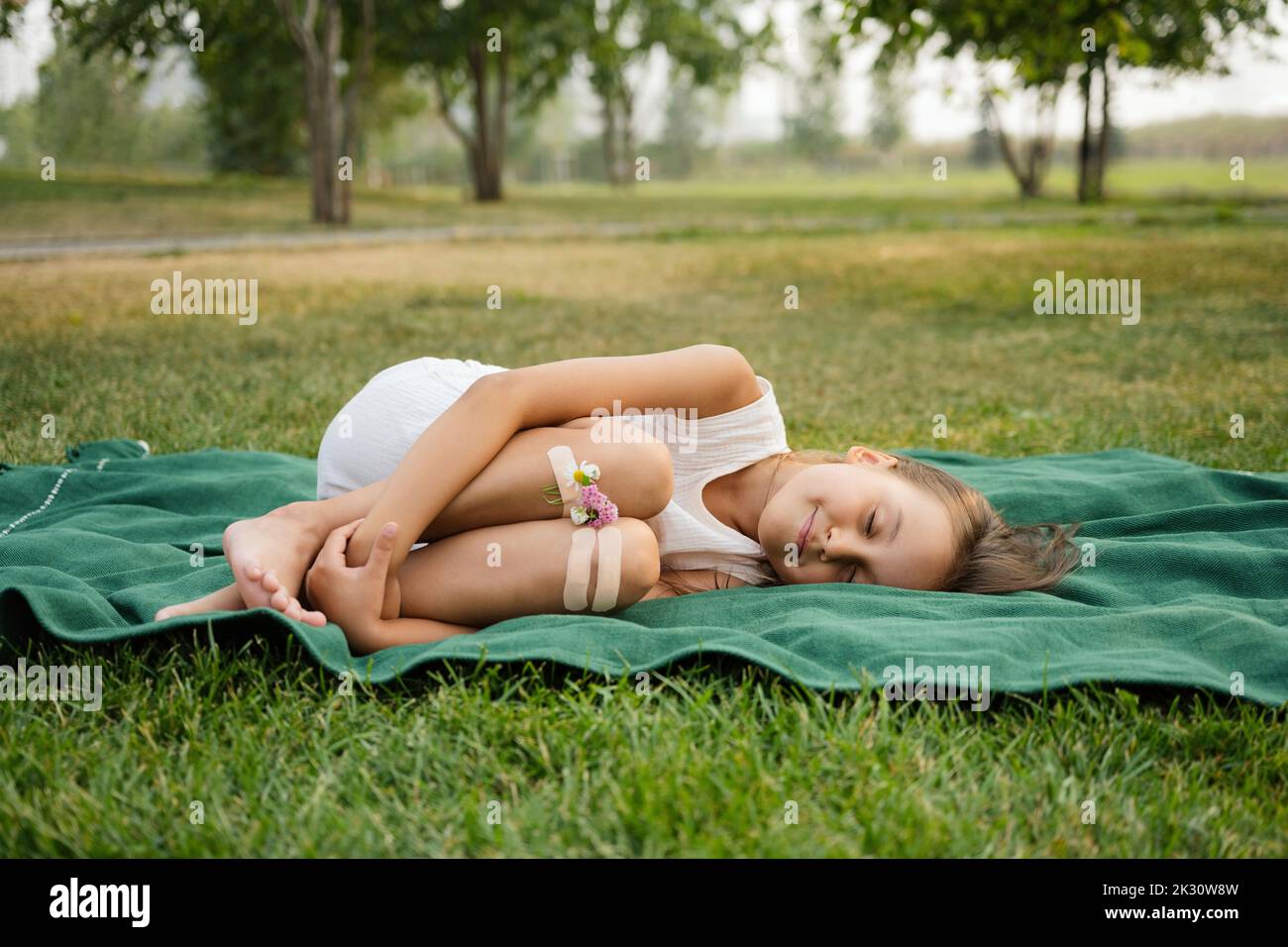 Fille avec des fleurs attachées aux genoux par bandage allongé sur une couverture au parc Banque D'Images