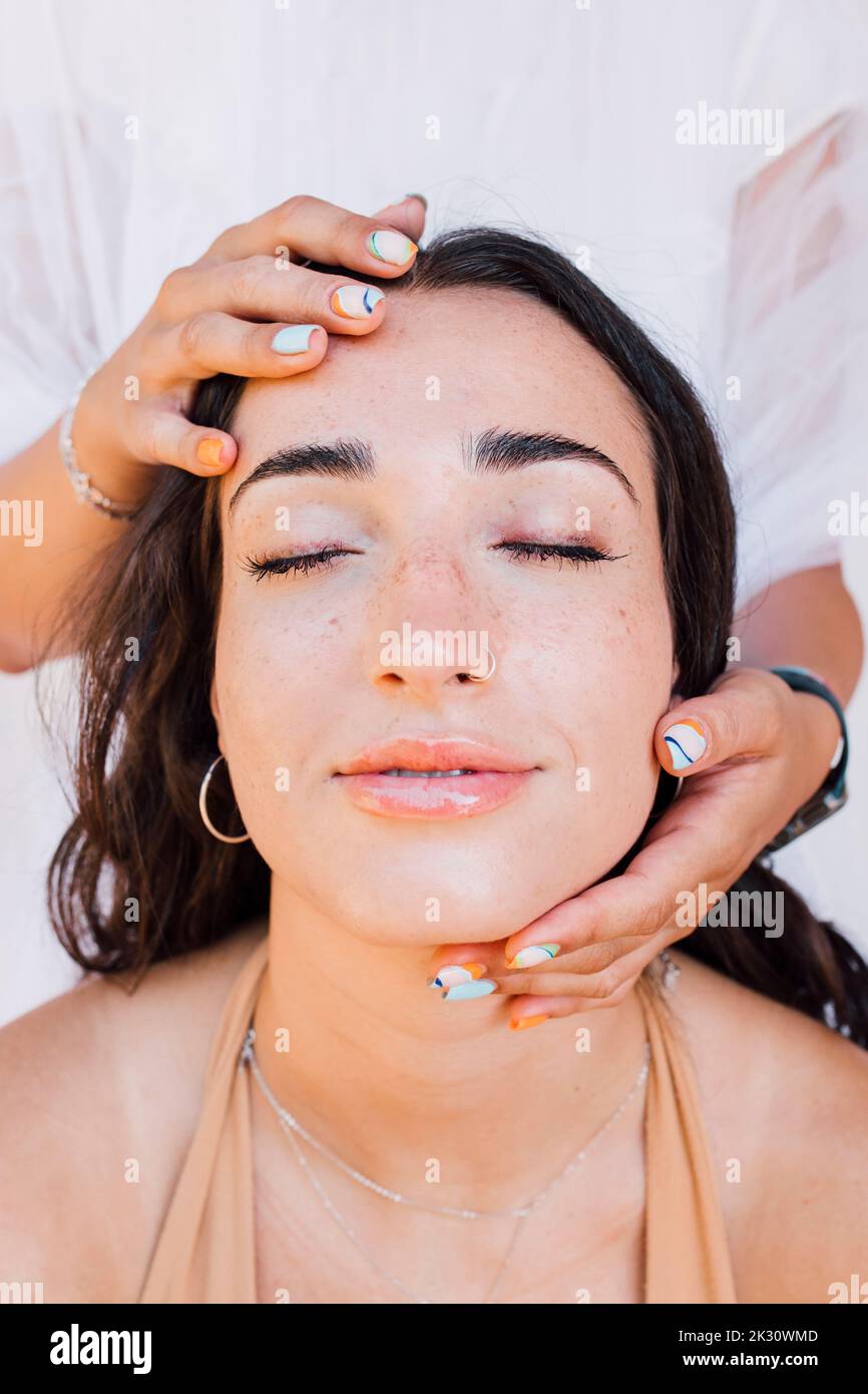 Mains touchant le visage de la belle jeune femme avec les yeux fermés Banque D'Images