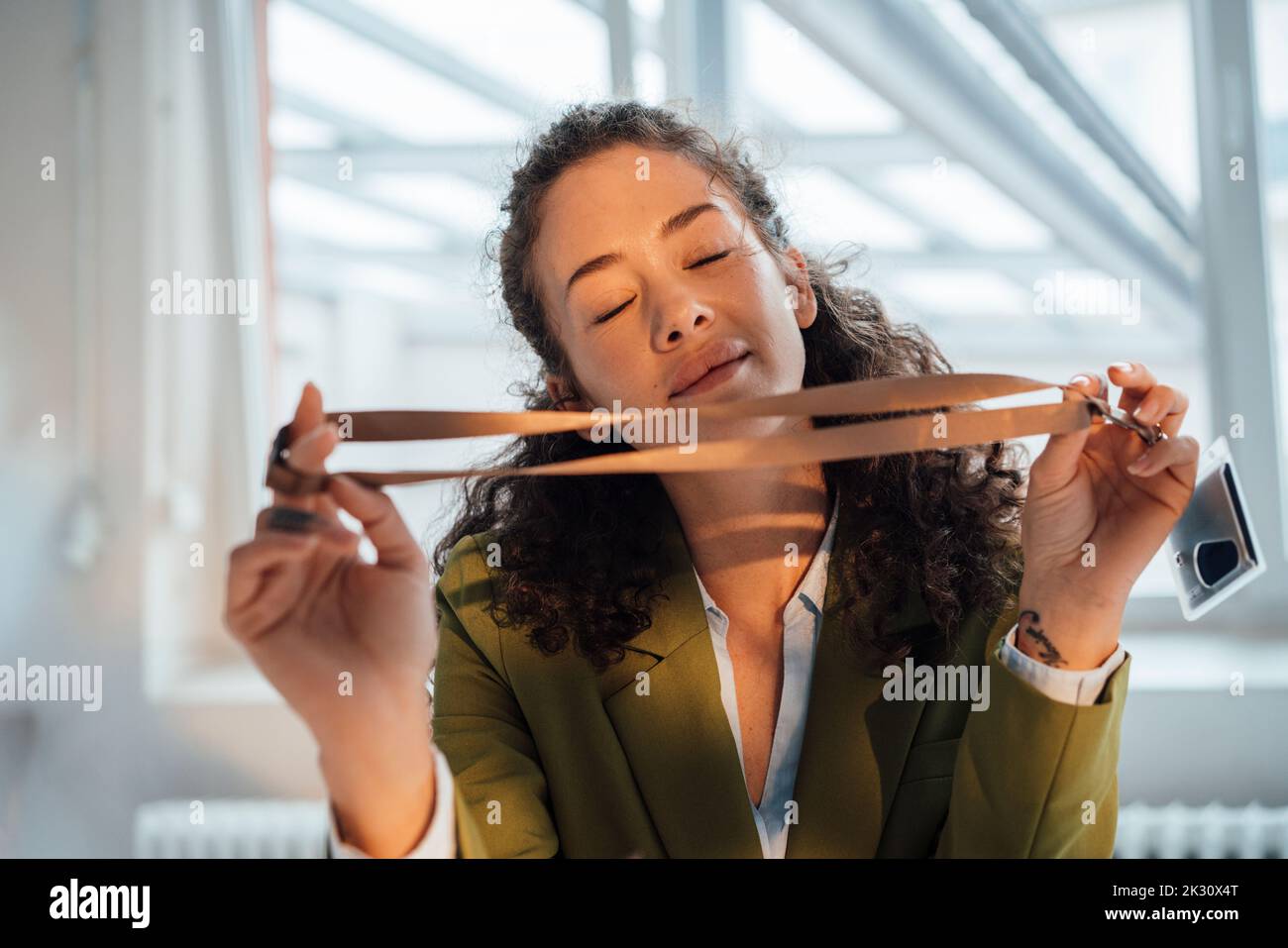 Femme d'affaires souriante avec les yeux fermés tenant la carte d'identité Banque D'Images