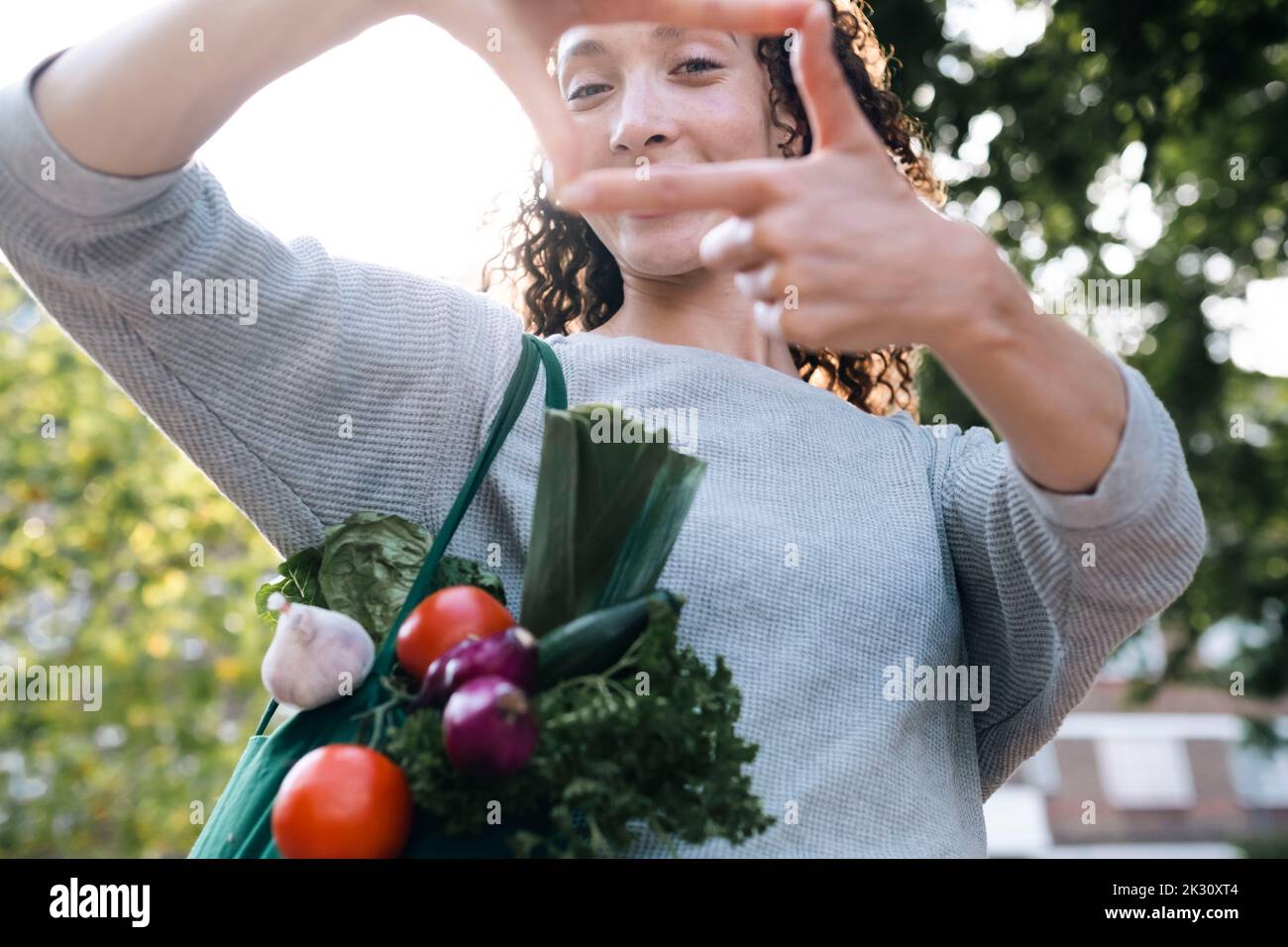 Femme avec sac de légumes regardant à travers le cadre de doigt Banque D'Images