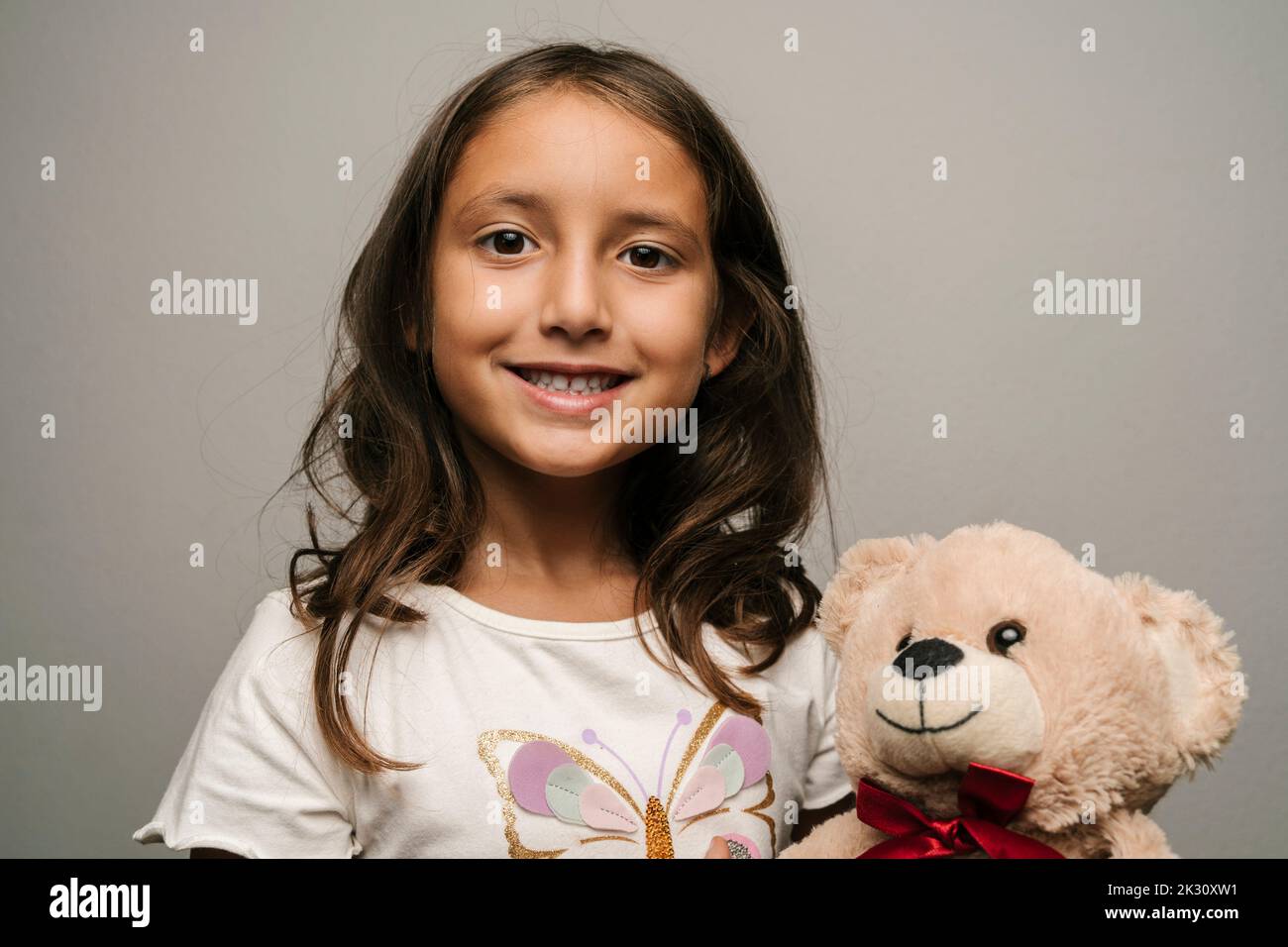 Fille souriante avec ours en peluche sur fond gris Banque D'Images
