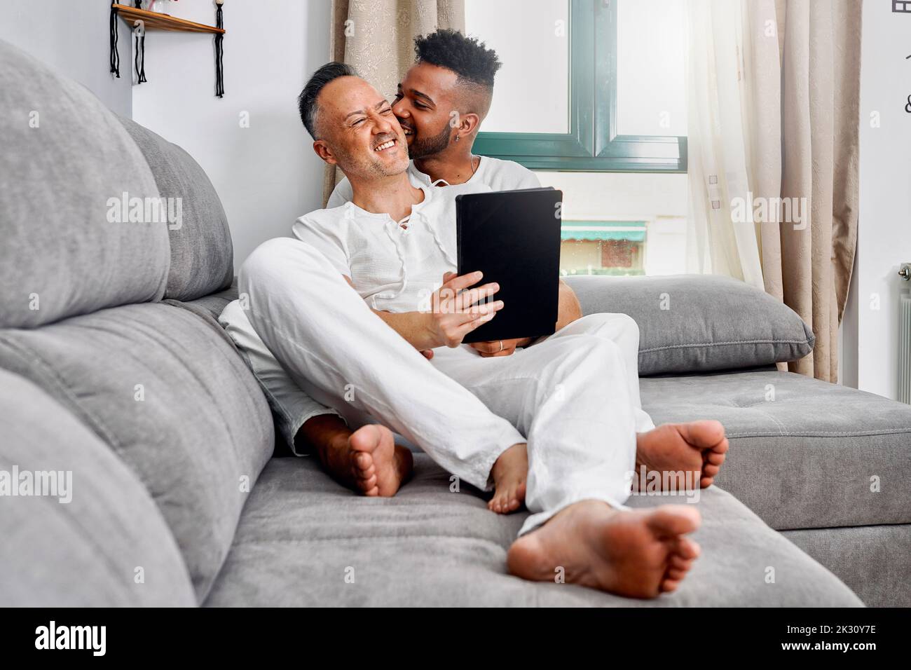 Jeune homme piquant l'oreille d'un petit ami assis sur un canapé à la maison Banque D'Images