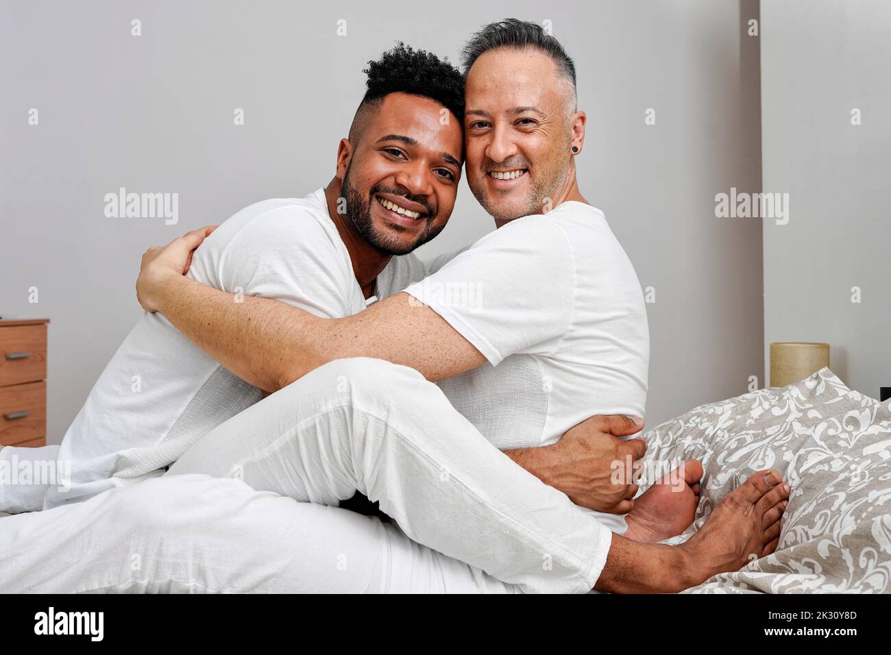 Happy gay couple embracing on bed at home Banque D'Images