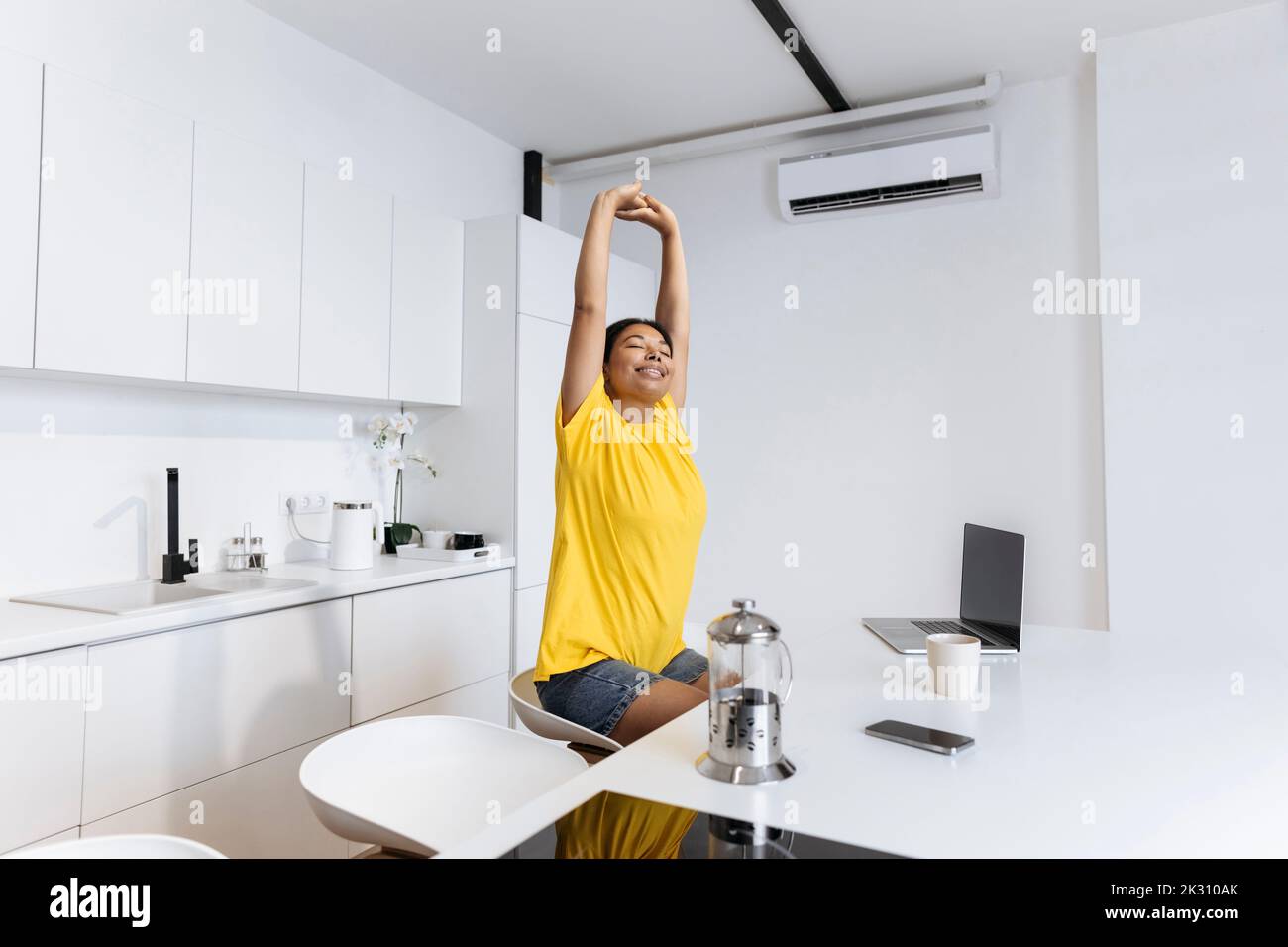 Une femme heureuse s'étirant dans la cuisine pour faire une pause dans le travail indépendant Banque D'Images