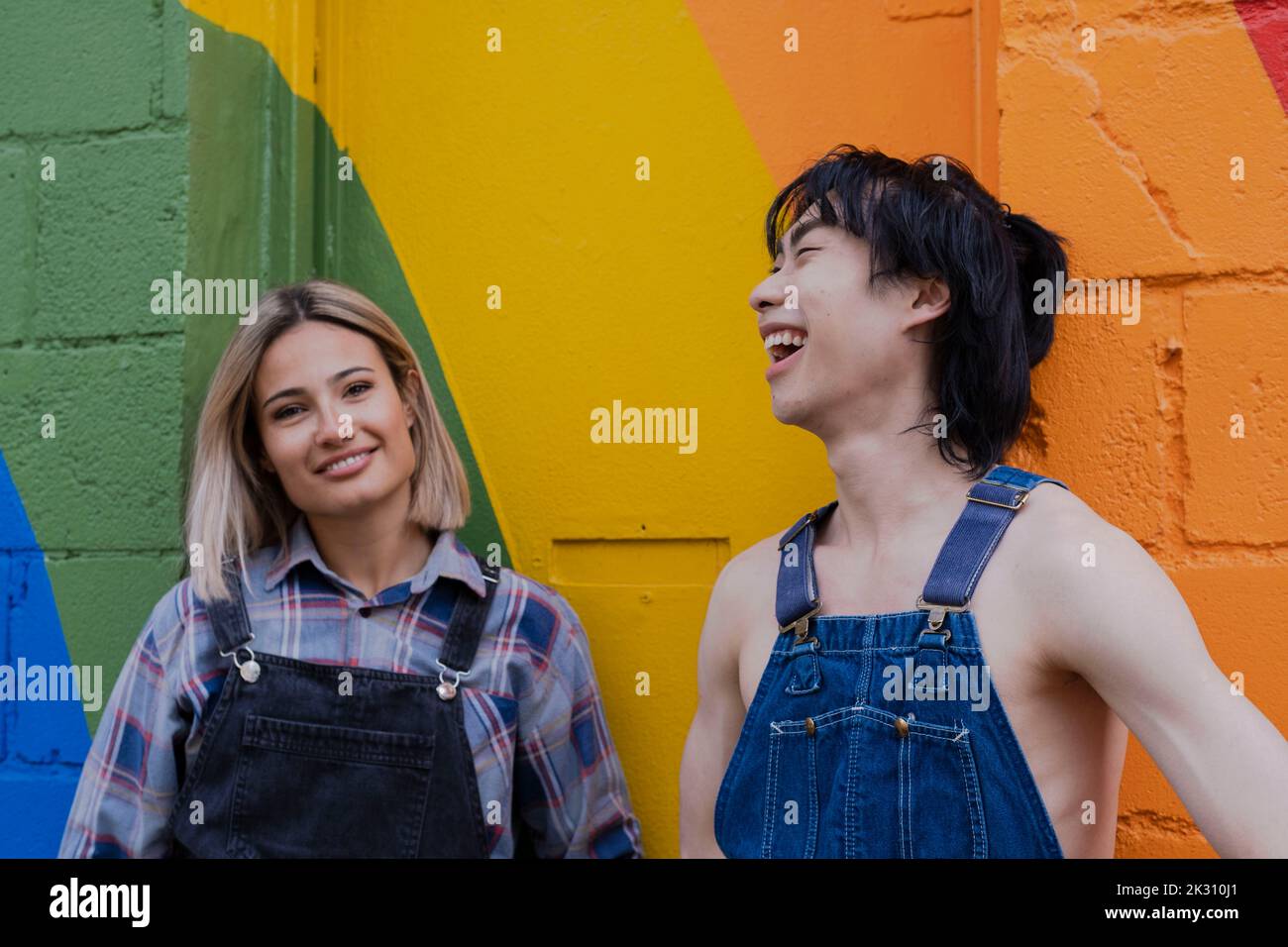 Young friends hanging out with each other standing in front of rainbow painted on wall Banque D'Images