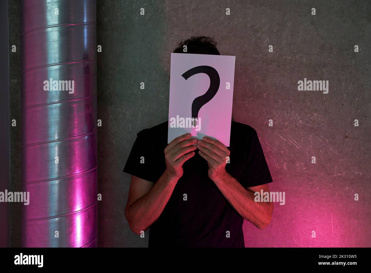 Homme tenant le signe de point d'interrogation sur le papier devant le mur Banque D'Images