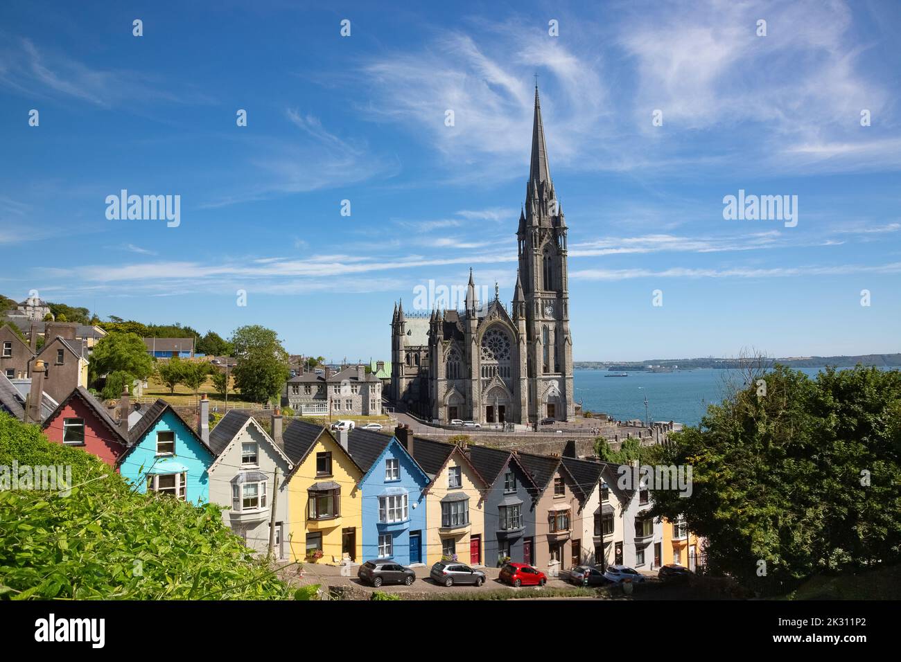 Irlande, Comté de Cork, Cobh, maisons en rangée colorées le long d'une rue escarpée avec la cathédrale Saint-Colmans en arrière-plan Banque D'Images