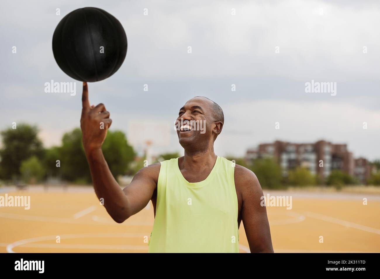 Homme souriant tournant le ballon sur le doigt debout sur le terrain de basket-ball Banque D'Images