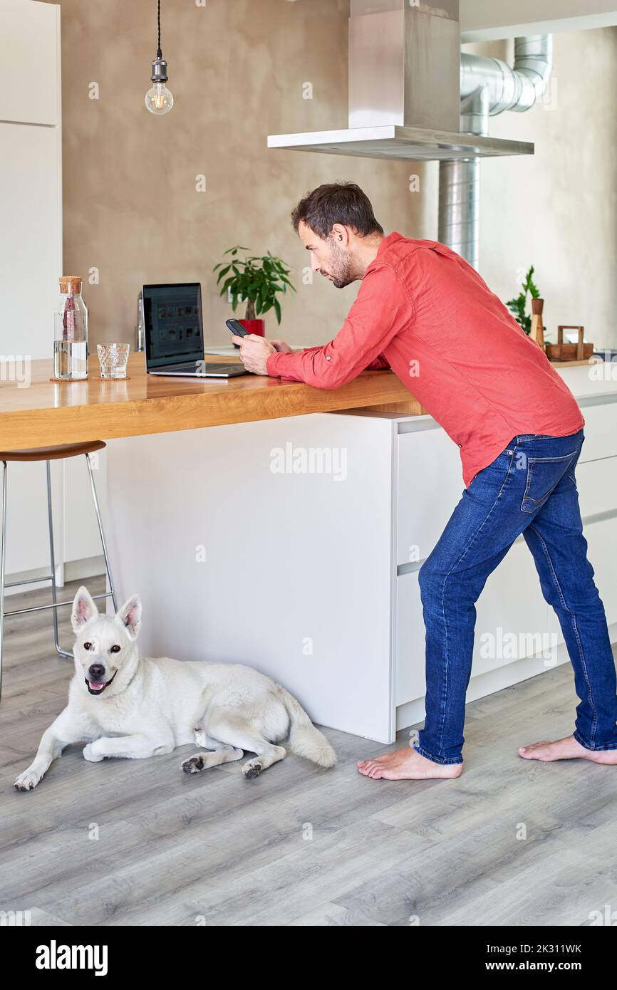 Homme qui utilise un smartphone et qui se penche sur une table à la maison Banque D'Images