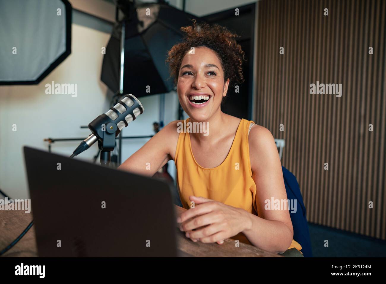 Un présentateur radio mûr riant par un microphone et un ordinateur portable sur une table en studio Banque D'Images