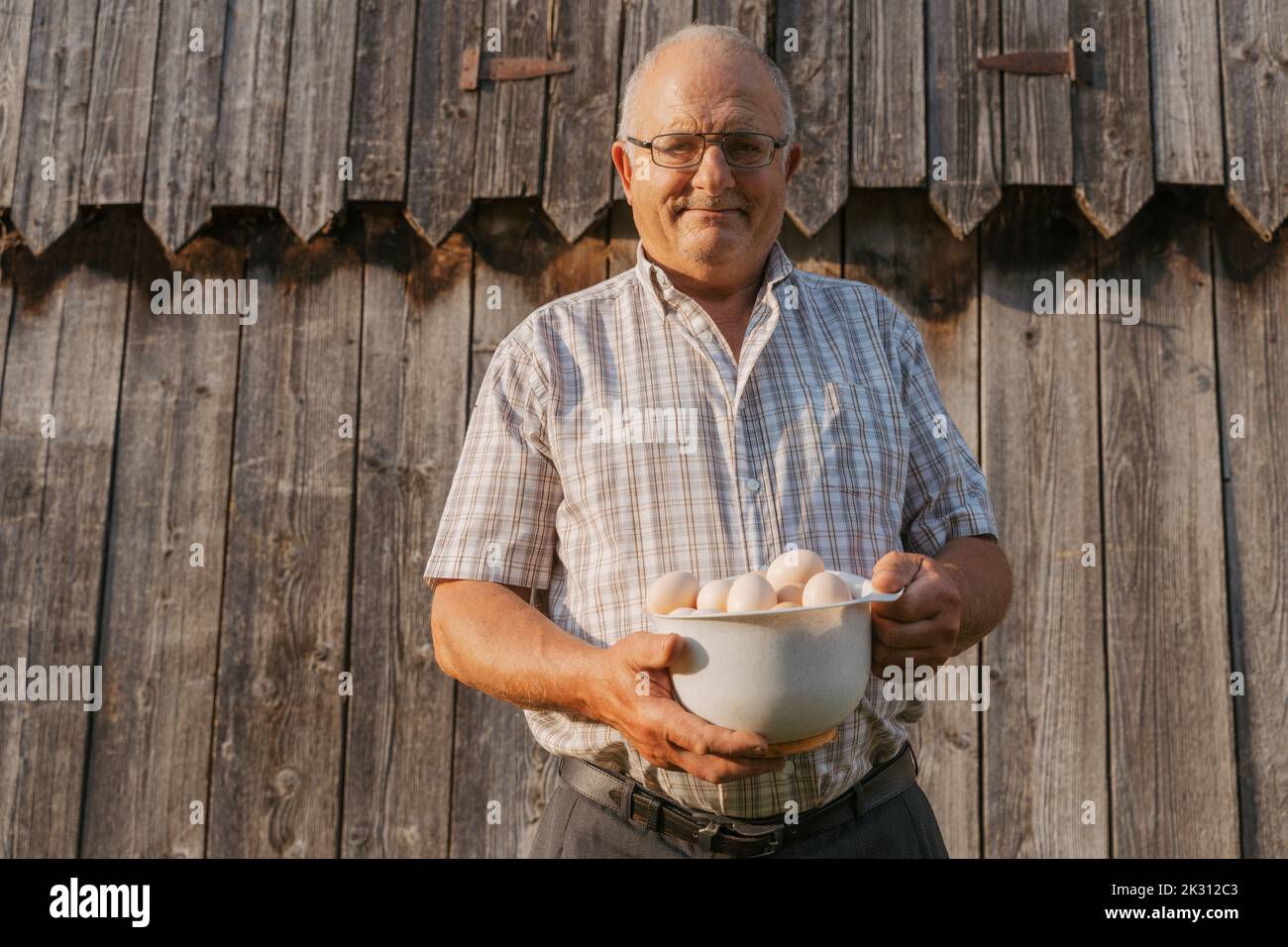 Agriculteur senior tenant un bol d'œufs le jour ensoleillé Banque D'Images