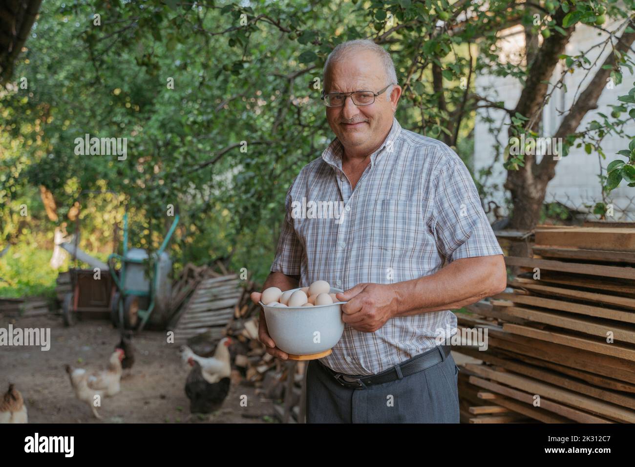 Fermier souriant tenant un bol d'œufs debout à la ferme Banque D'Images