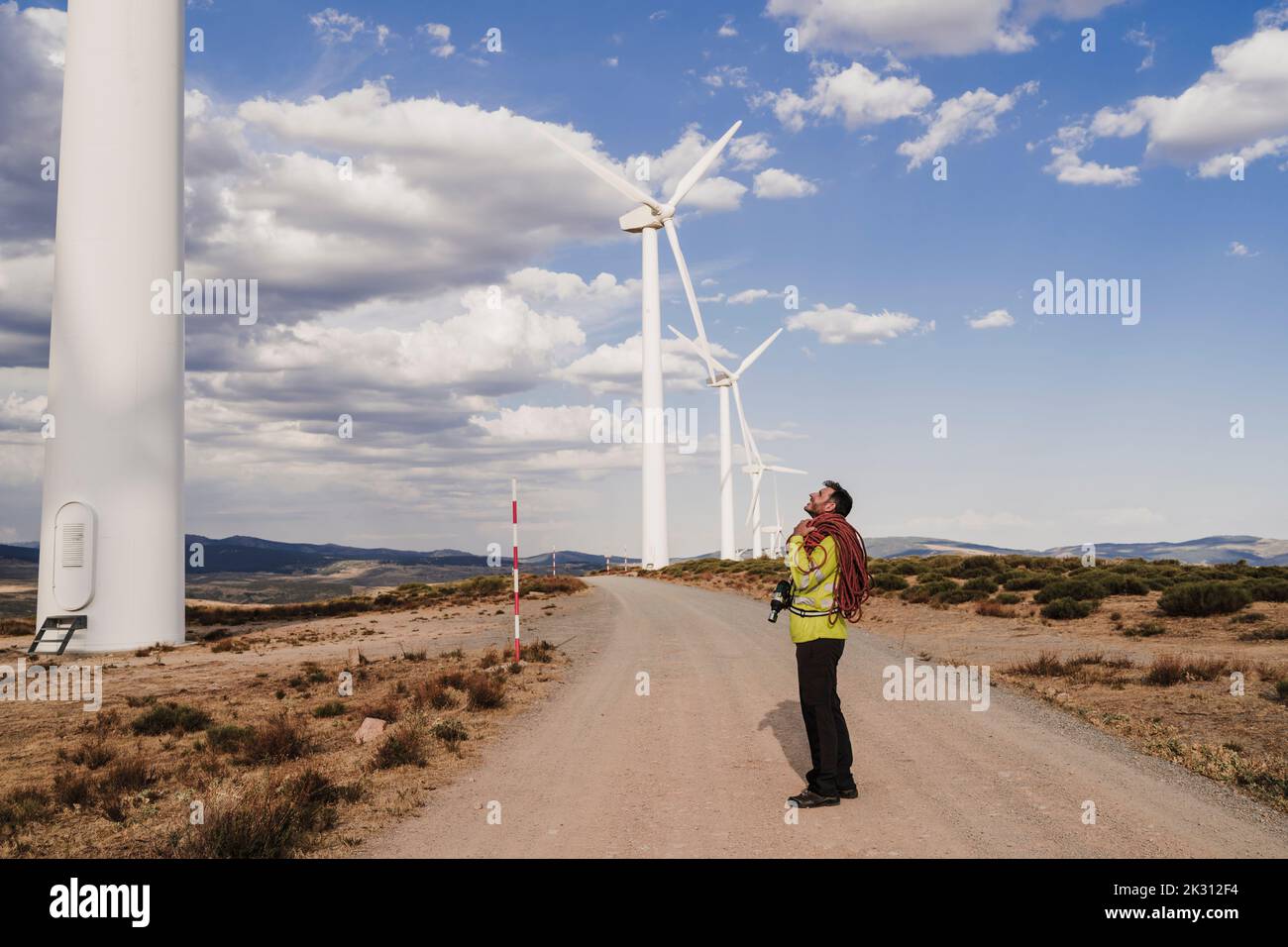 Technicien avec corde debout sur la route regardant l'éolienne Banque D'Images