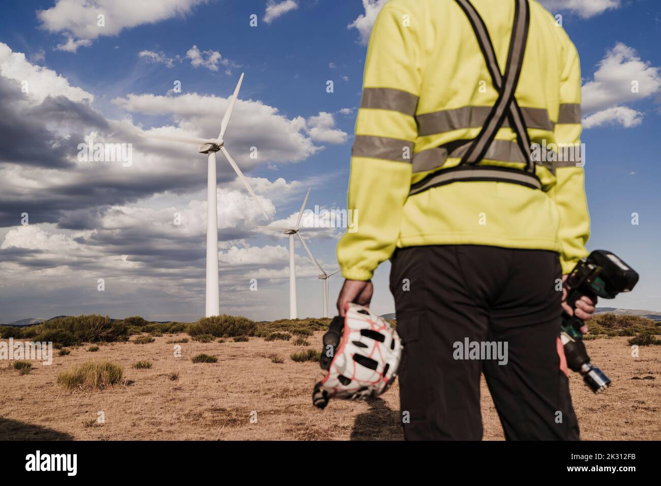 Technicien tenant l'outil de travail et le casque debout à la ferme éolienne Banque D'Images