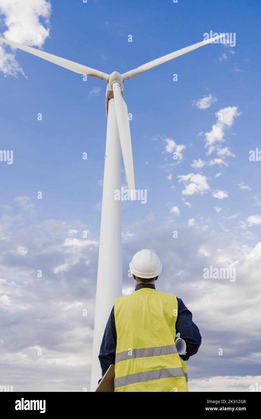 Ingénieur portant des vêtements réfléchissants regardant la grande éolienne Banque D'Images