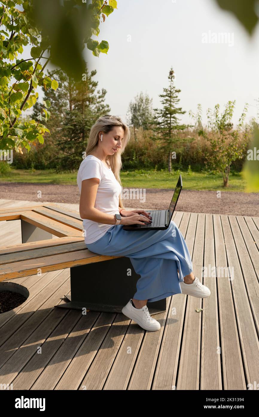 Indépendant travaillant sur un ordinateur portable assis sur un banc dans le parc Banque D'Images
