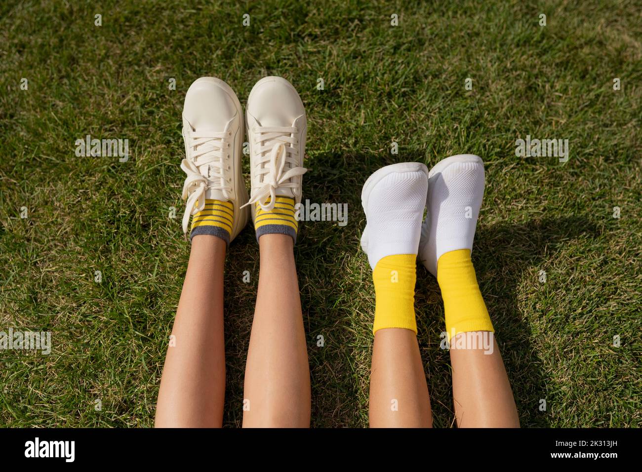 Les filles portant des chaussures blanches se détendent sur l'herbe au parc Banque D'Images