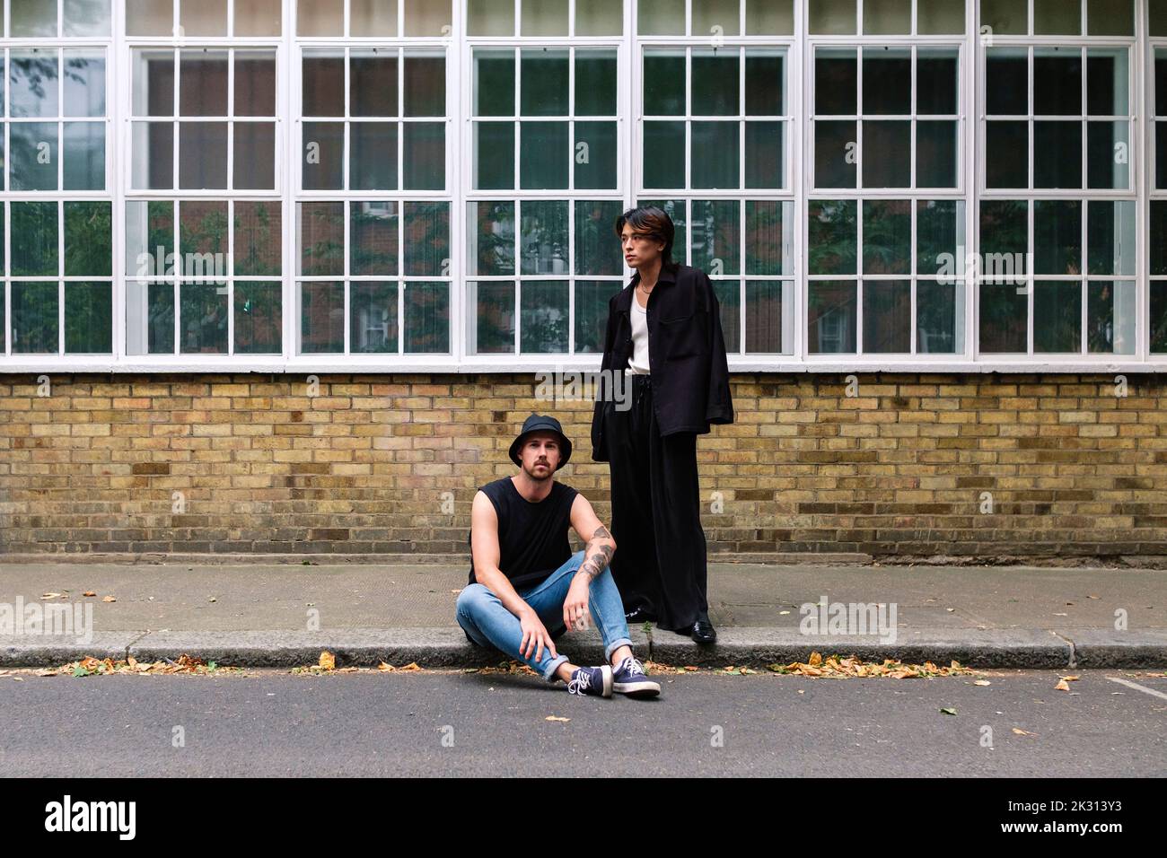 Jeune homme debout près d'un petit ami assis sur le trottoir Banque D'Images