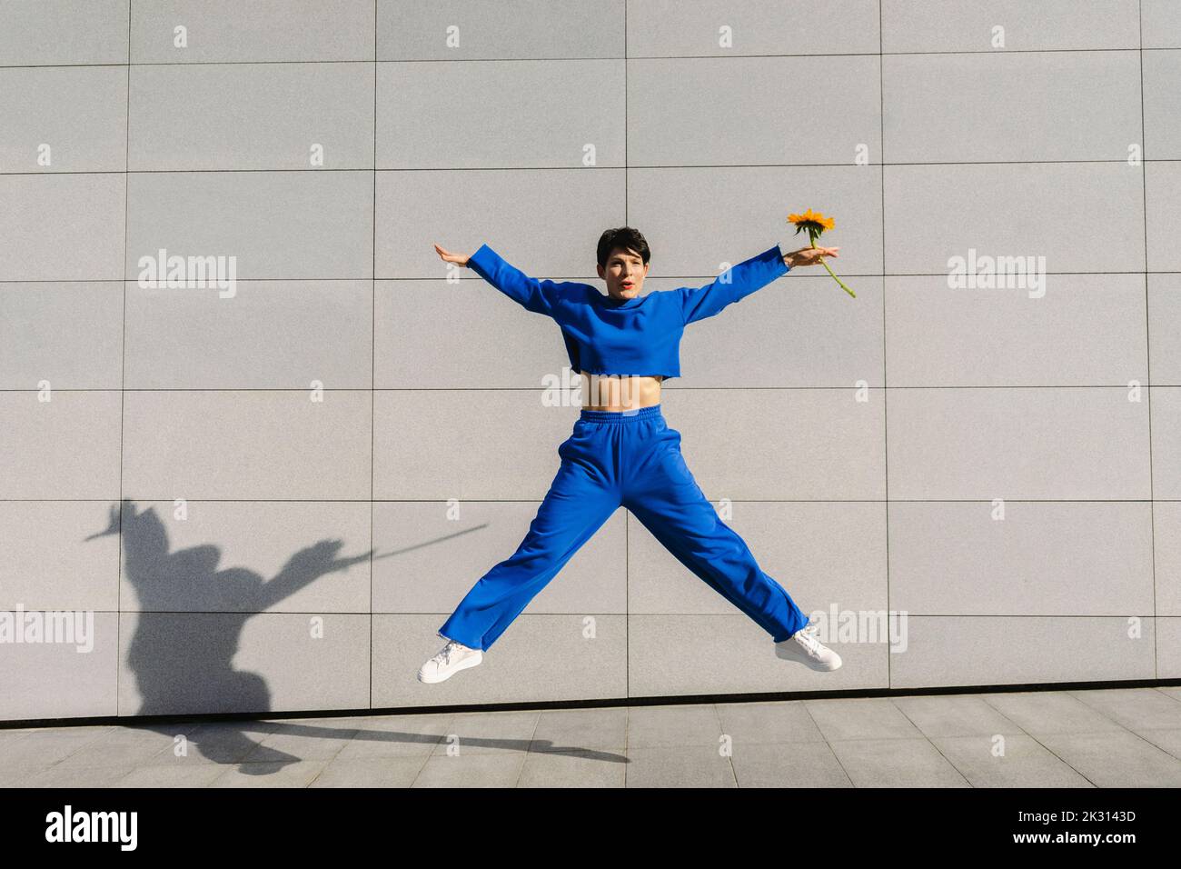 Femme active avec les bras débordés sautant devant le mur le jour ensoleillé Banque D'Images