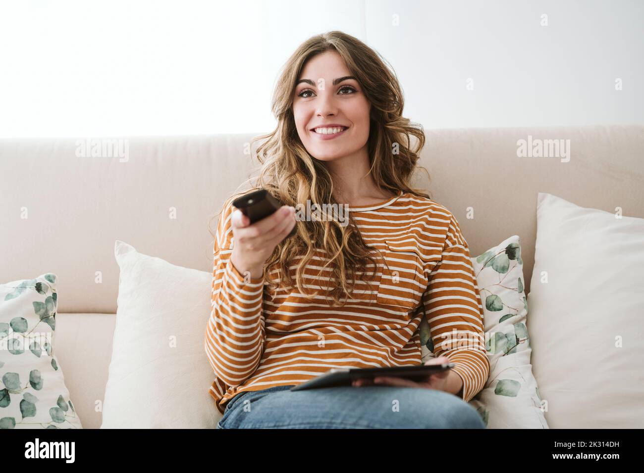 Jeune femme utilisant la télécommande sur le canapé à la maison Banque D'Images