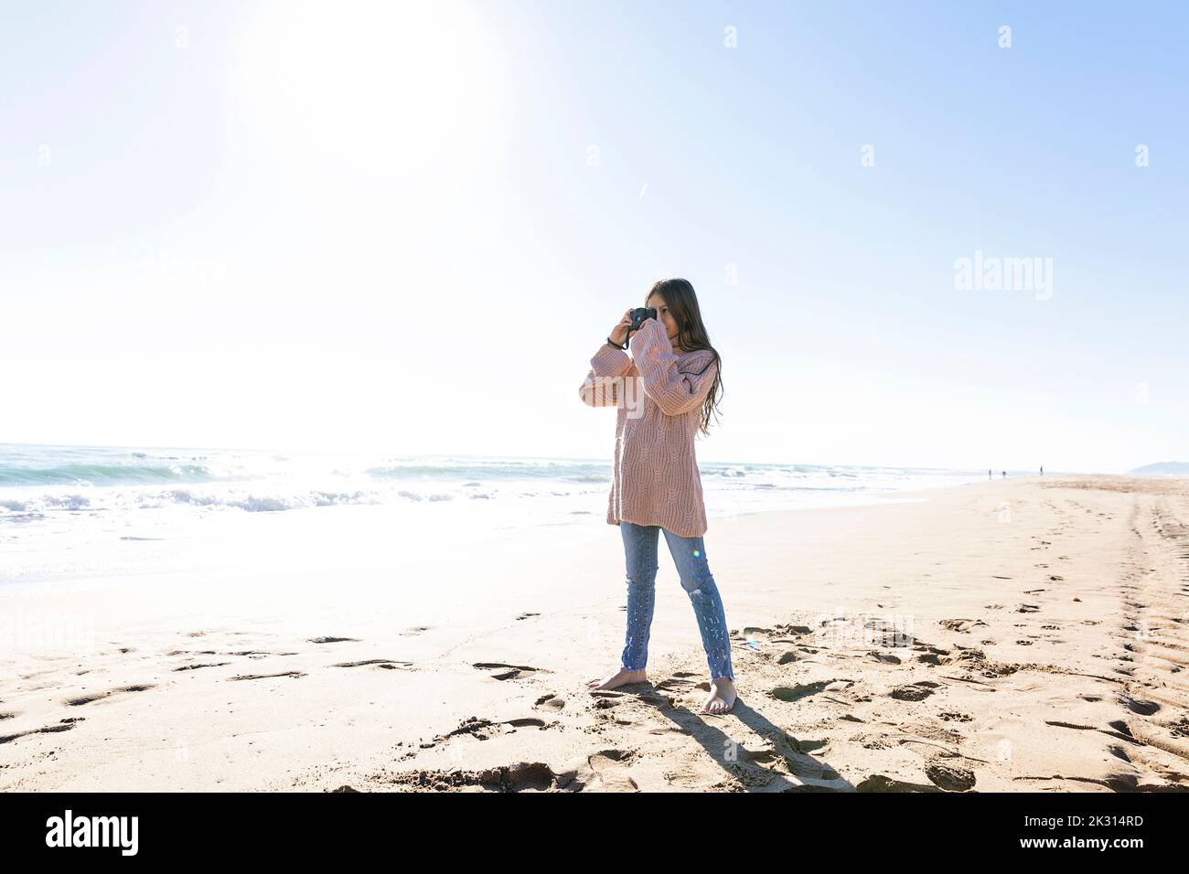 Fille debout avec un appareil photo prenant des photos à la plage Banque D'Images