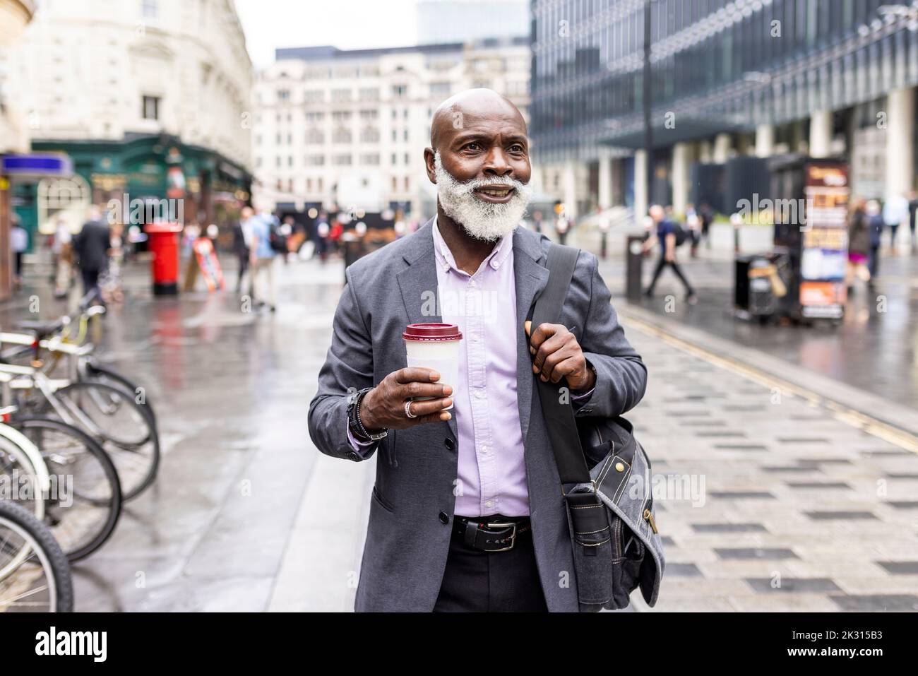 Homme d'affaires souriant avec une tasse à café jetable sur le sentier Banque D'Images