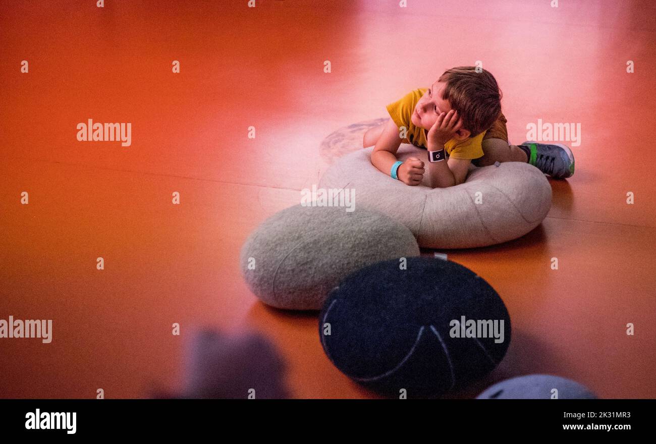 Un garçon allongé sur des coussins avec pose contemplative sur le sol à Eurospace Centre, Libin, Belgique Banque D'Images