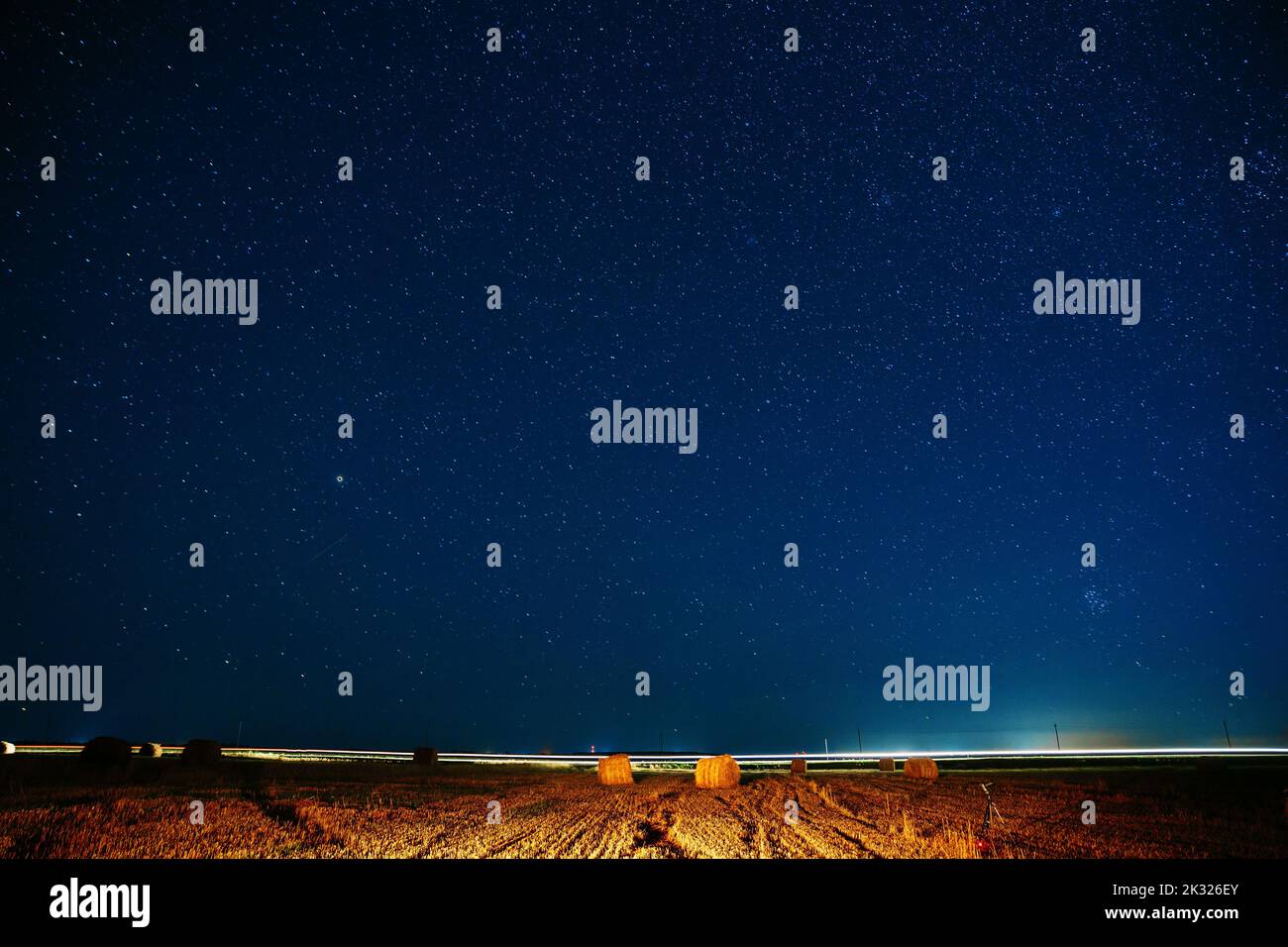 Espace de copie d'arrière-plan agricole coloré. Ciel étoilé de nuit au-dessus du paysage rural champ de prairie avec rouleaux de paille dans les champs après récolte. Brillant Banque D'Images