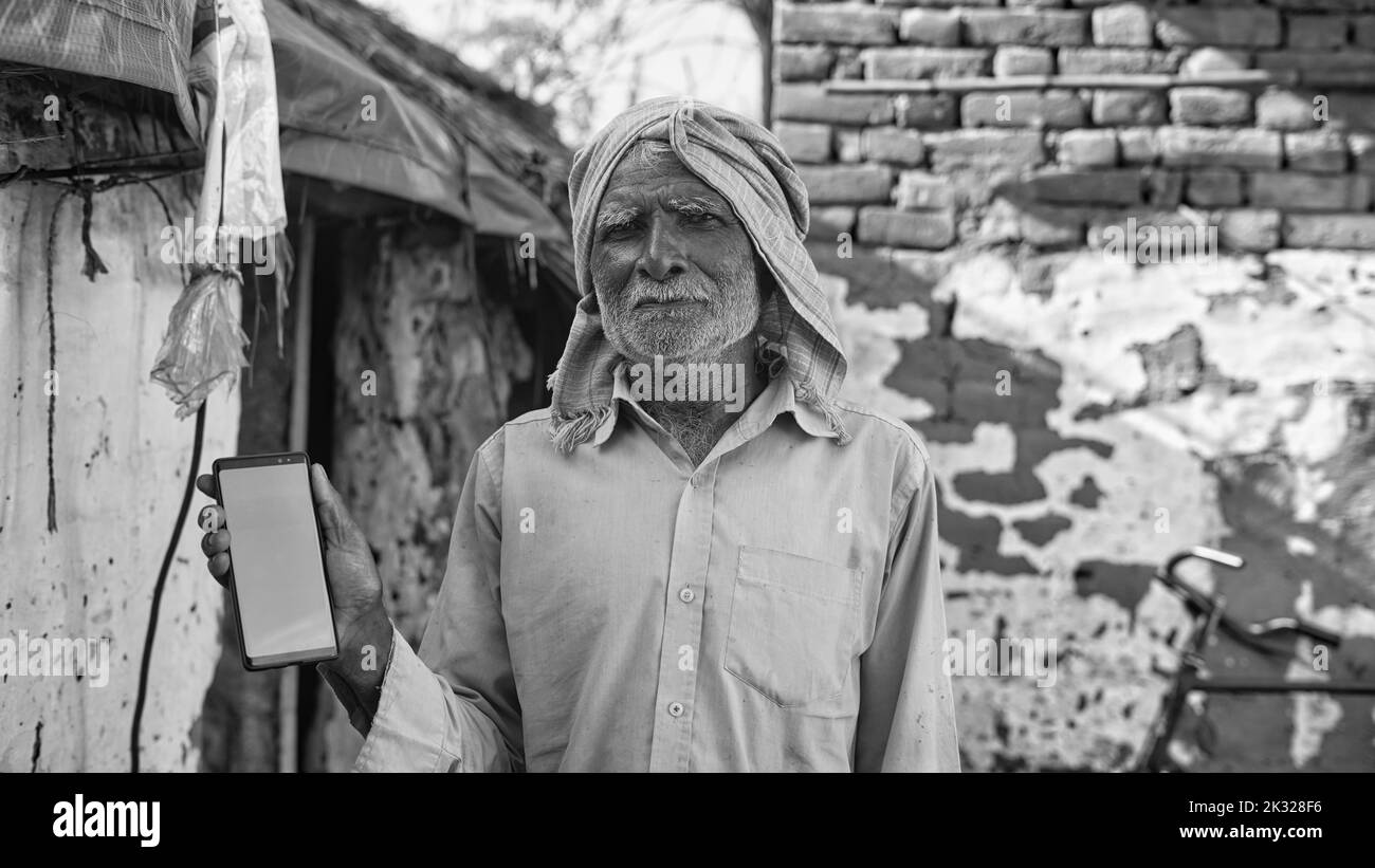 Vieil homme asiatique souriant et montrant un téléphone cellulaire à écran vert avec fond de concept de vie de village rural. Banque D'Images