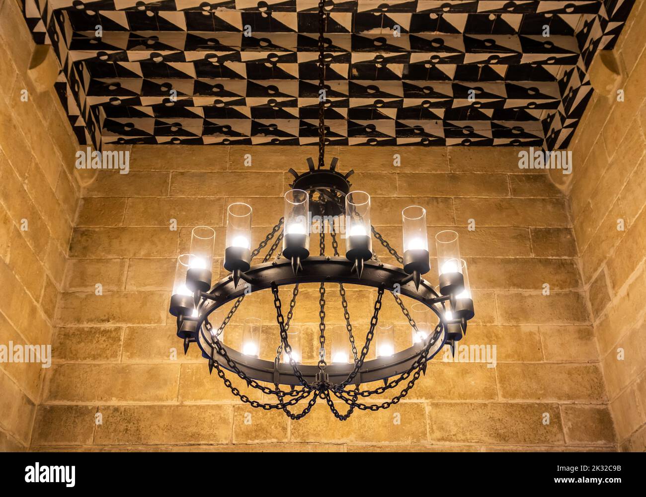 Ancienne lampe en fer forgé noir accrochée à un plafond en bois dans une salle en pierre Banque D'Images