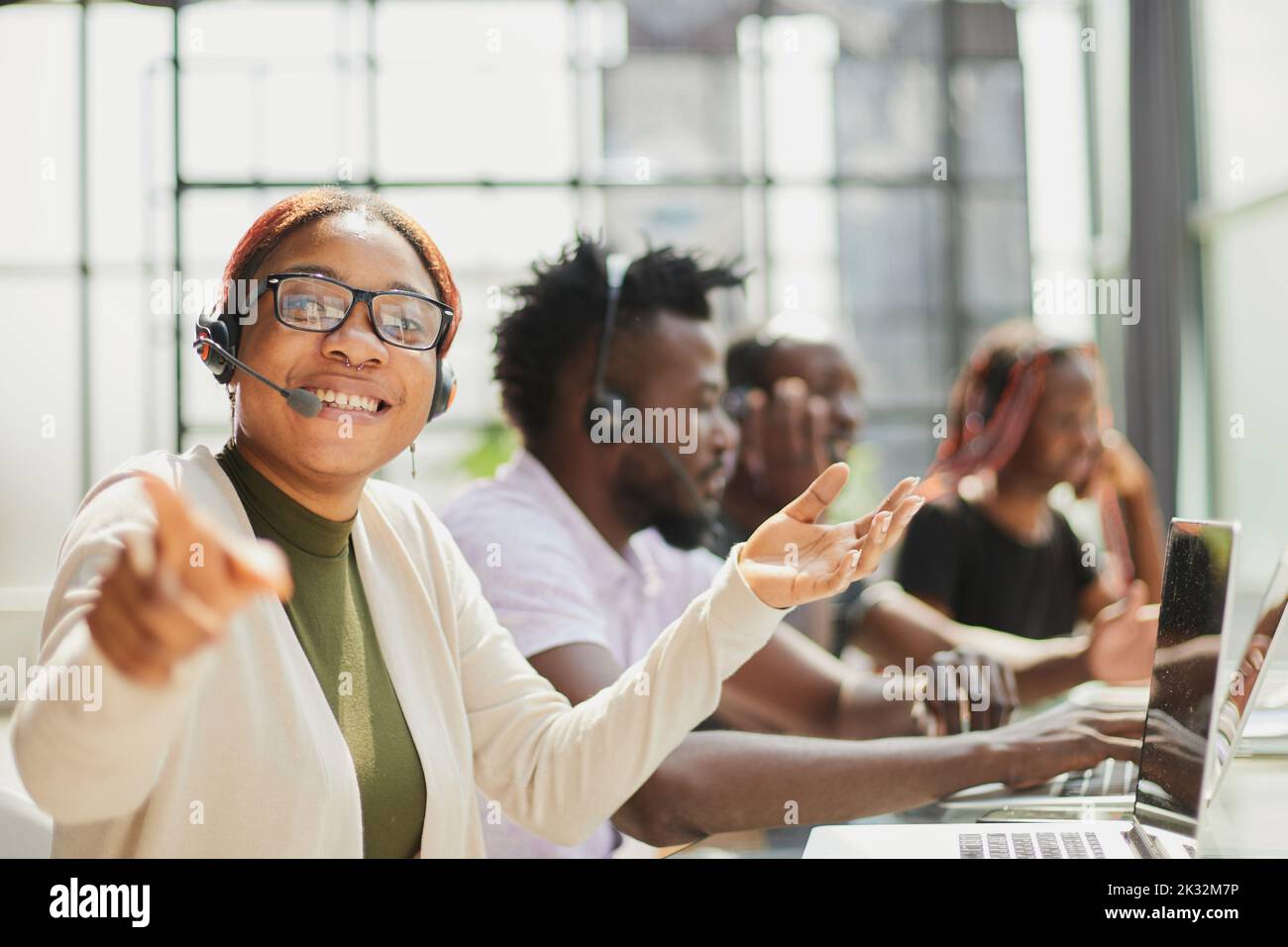 Belle femme afro-américaine souriante travaillant dans un centre d'appels avec une équipe diversifiée Banque D'Images