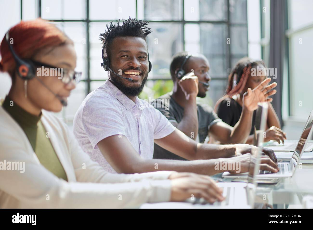 Belle femme afro-américaine souriante travaillant dans un centre d'appels avec une équipe diversifiée Banque D'Images