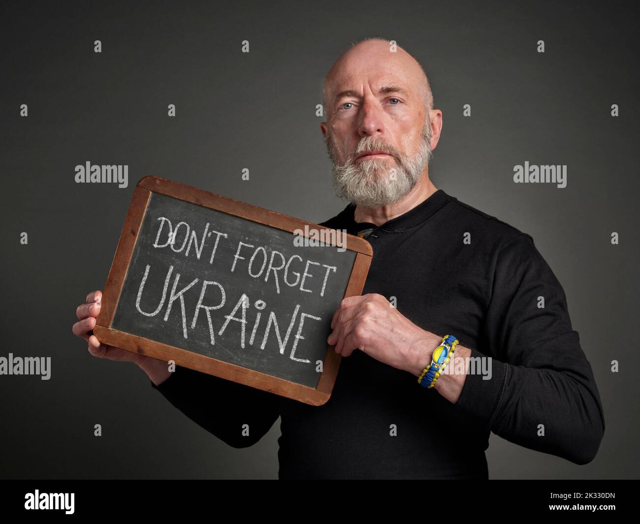 N'oubliez pas l'Ukraine - des mots en craie blanche sur un tableau noir d'ardoise tenu par un homme âgé portant un bracelet bleu et jaune Banque D'Images