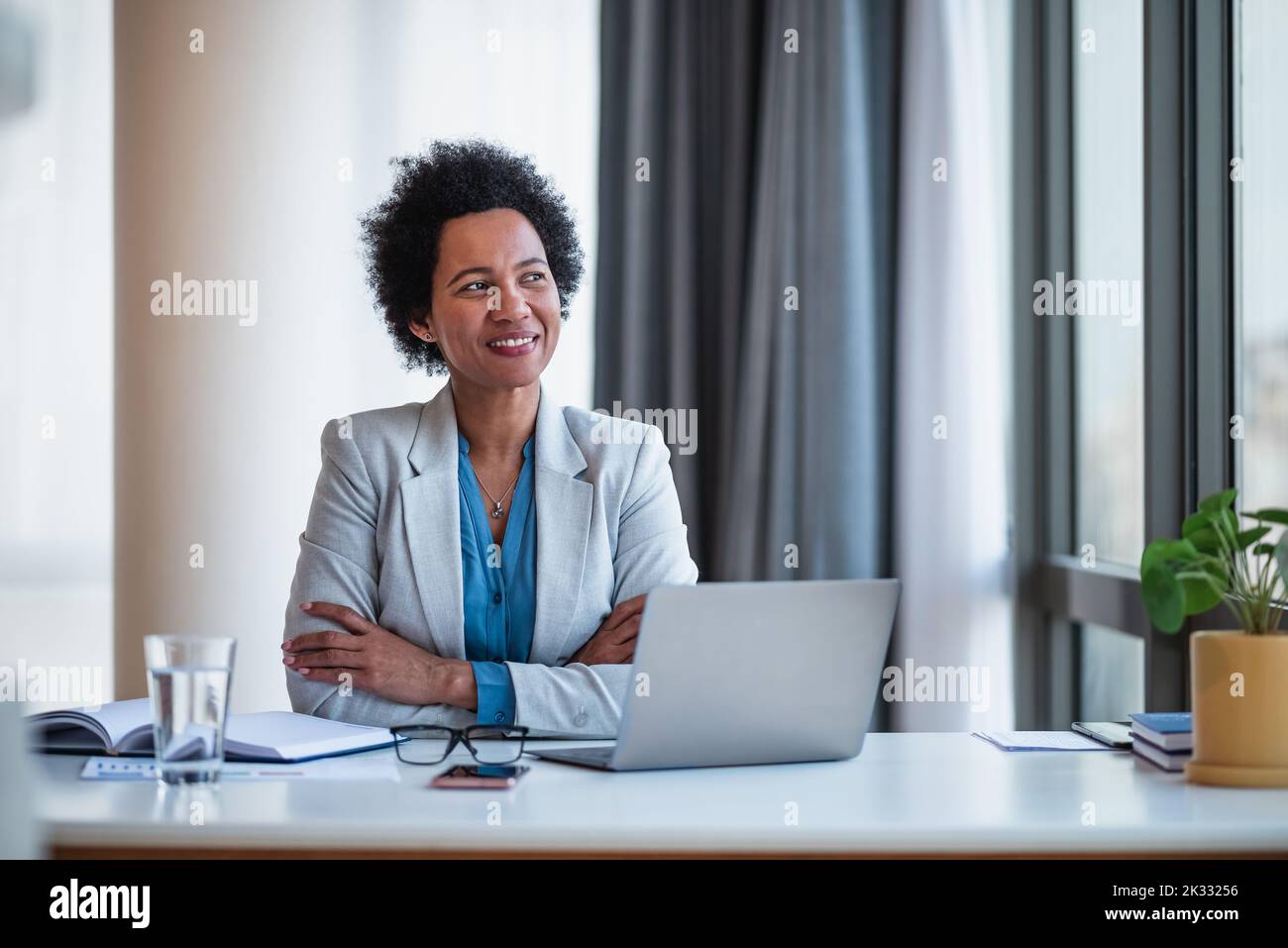 Photo d'une femme afro-américaine confiante, assise dans son bureau, regardant à l'extérieur. Banque D'Images
