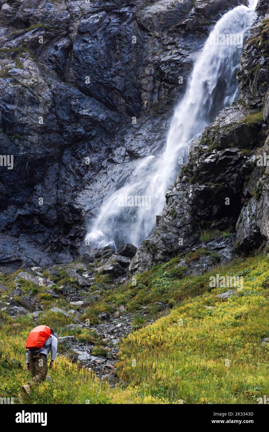 Un homme va jusqu'aux montagnes avec une chute d'eau non concentrée et des rochers comme arrière-plan. Scène de voyage en montagne Banque D'Images