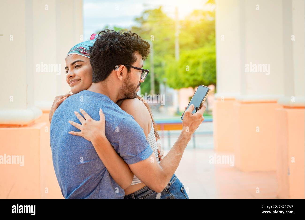 Un petit ami infidèle qui embrasse sa petite amie et regarde le téléphone portable. Concept de l'homme infidèle utilisant le téléphone cellulaire. Homme infidèle regardant le Banque D'Images