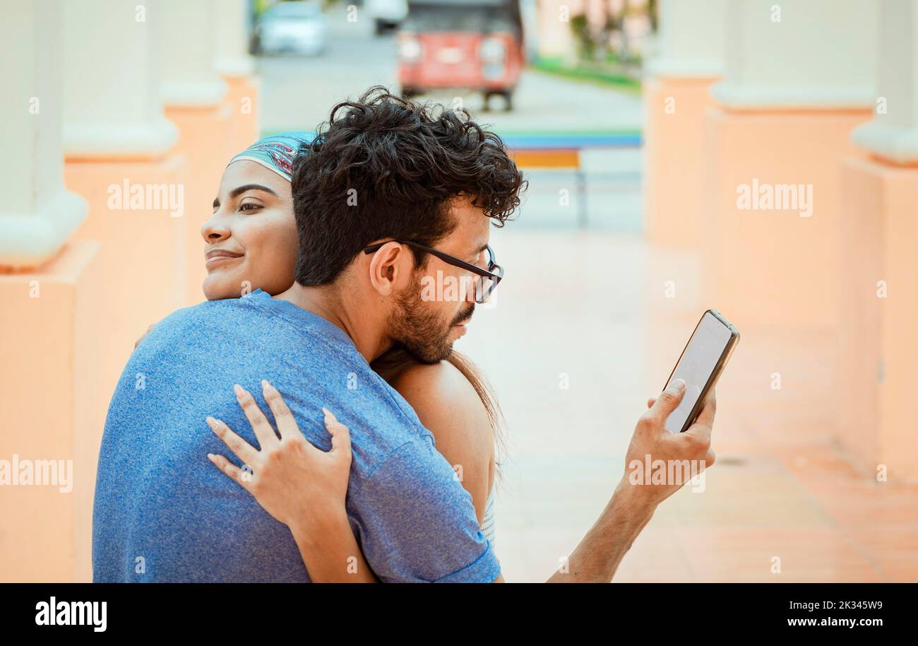 Homme infidèle regardant le téléphone portable tout en embrassant sa petite amie à l'extérieur. Un petit ami infidèle embrassant sa petite amie et regardant la cellule Banque D'Images