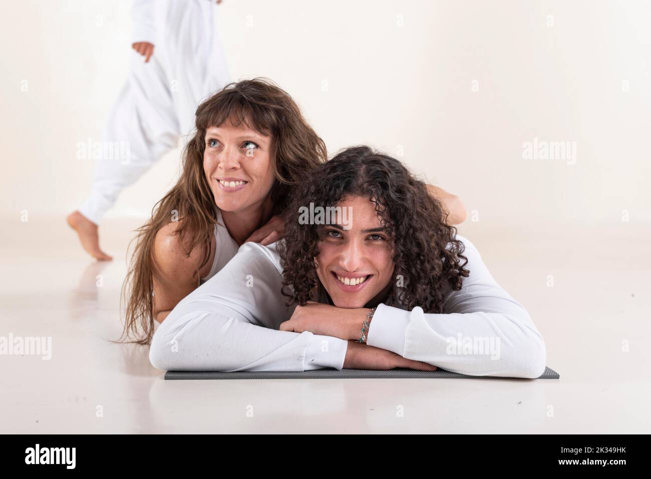 Portrait d'un jeune homme vêtu de vêtements blancs de yoga allongé sur un tapis tout en regardant l'appareil photo avec un ami sur fond blanc. Prise de vue en studio Banque D'Images