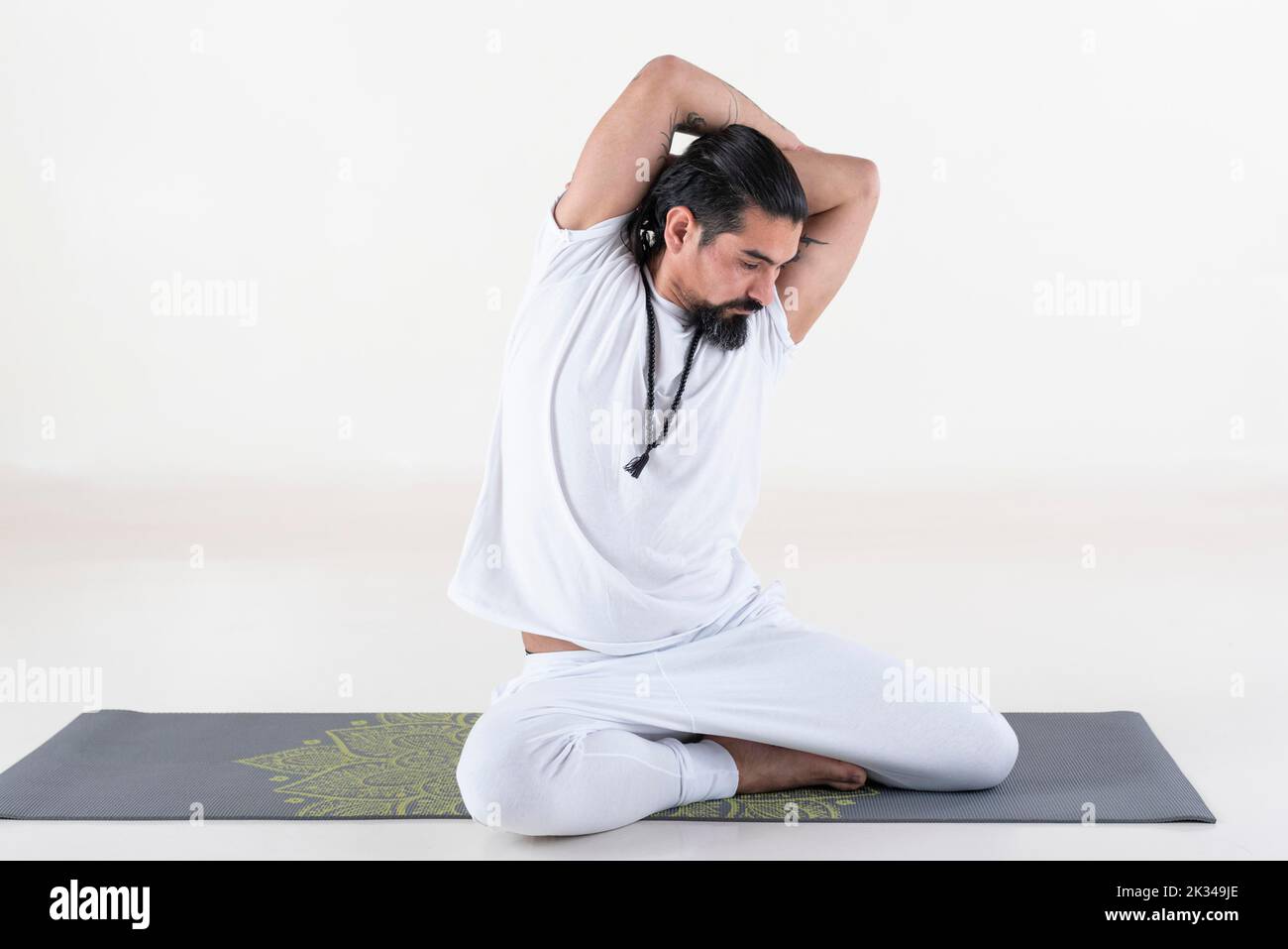 Un homme vêtu de blanc faisant du yoga sur un tapis sur fond blanc. Bharadvajasana pose de yoga. Prise de vue en studio Banque D'Images