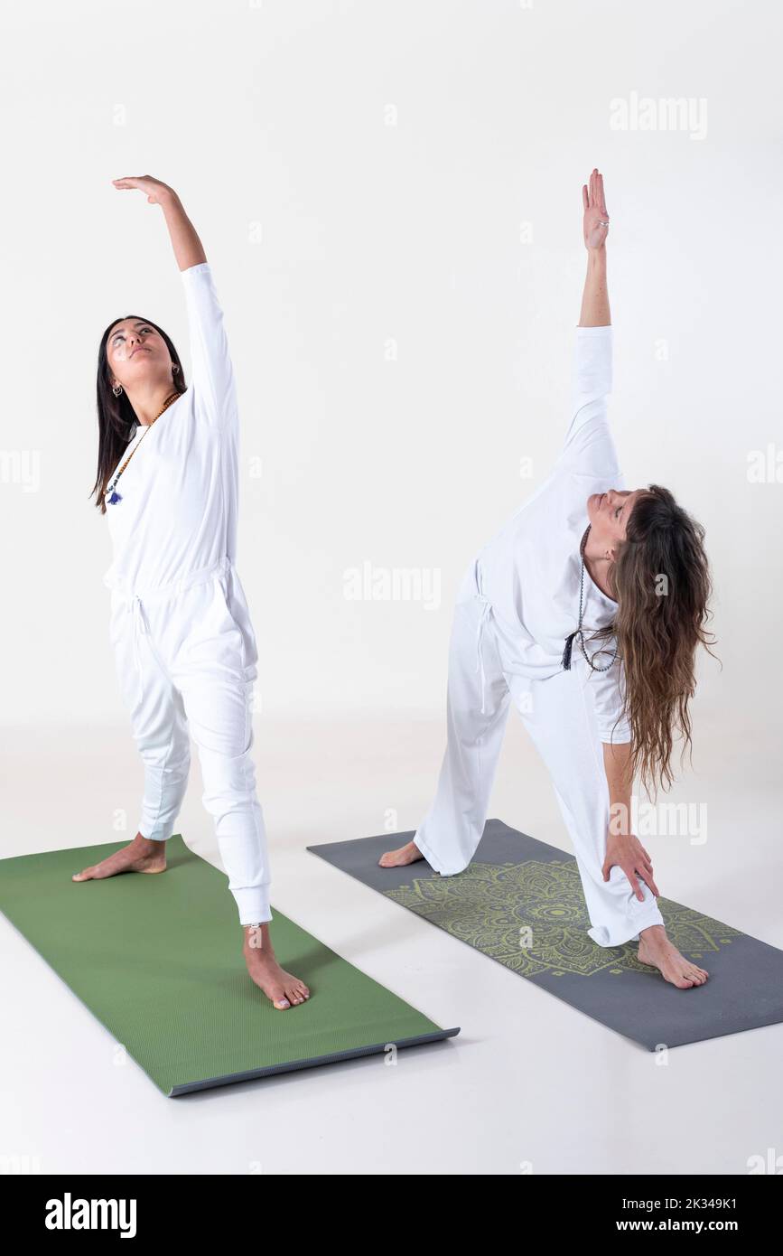 Deux femmes vêtues de blanc faisant du yoga sur fond blanc. Posture du yoga Utthita trikonasana. Prise de vue en studio Banque D'Images