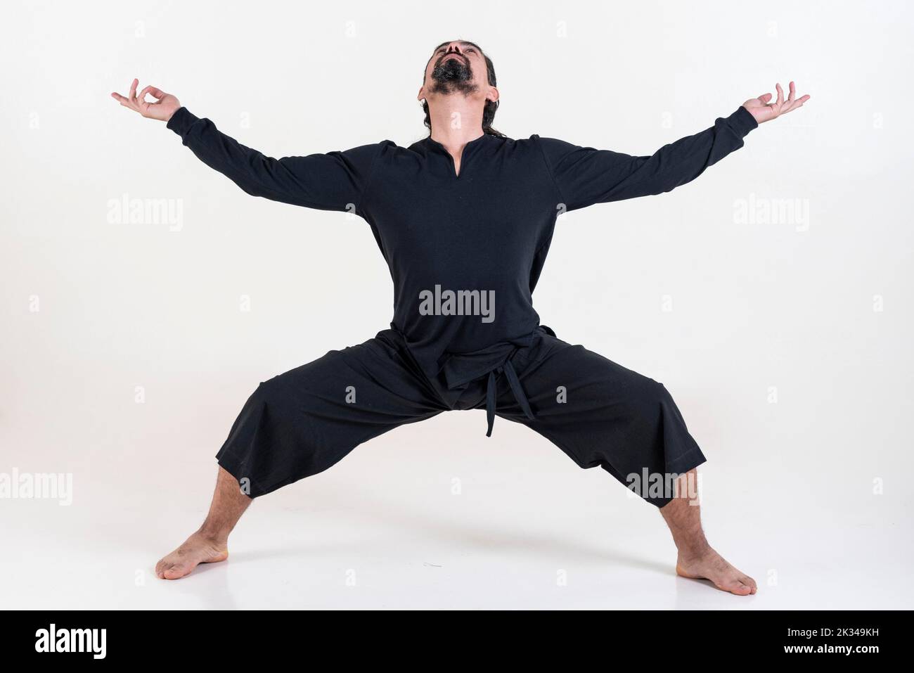 Un homme vêtu de noir faisant du yoga sur fond blanc. Utkata konasana pose de yoga. Prise de vue en studio Banque D'Images