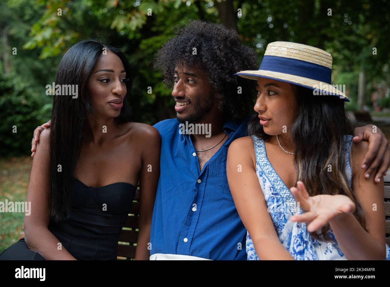 Trois amis multiraciaux souriants assis sur le banc du parc font le contact visuel. Banque D'Images