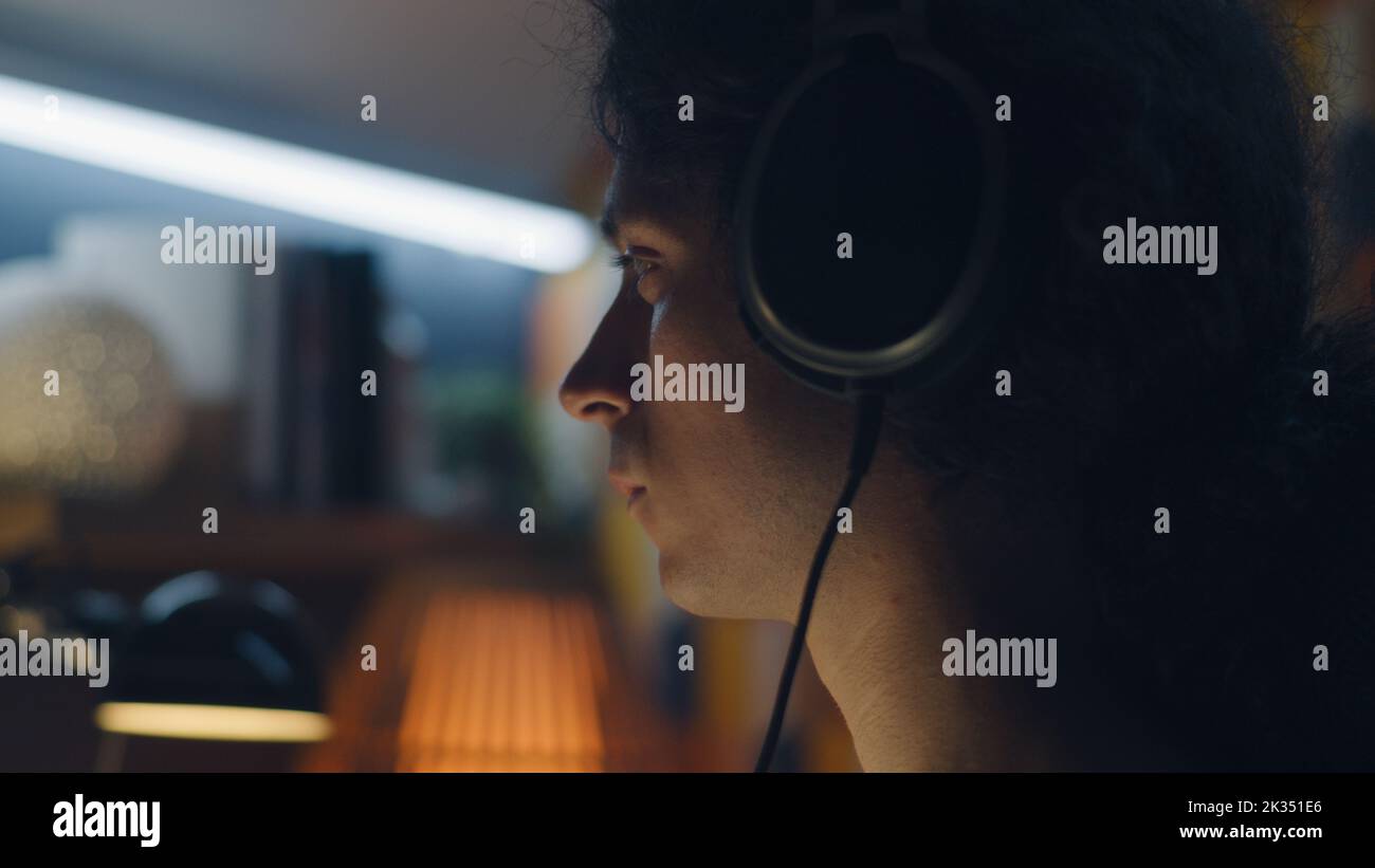 Homme dans le casque de navigation sur Internet et les réseaux sociaux sur ordinateur à la maison la nuit et d'écouter de la musique ou d'avoir en ligne freelance travail Banque D'Images